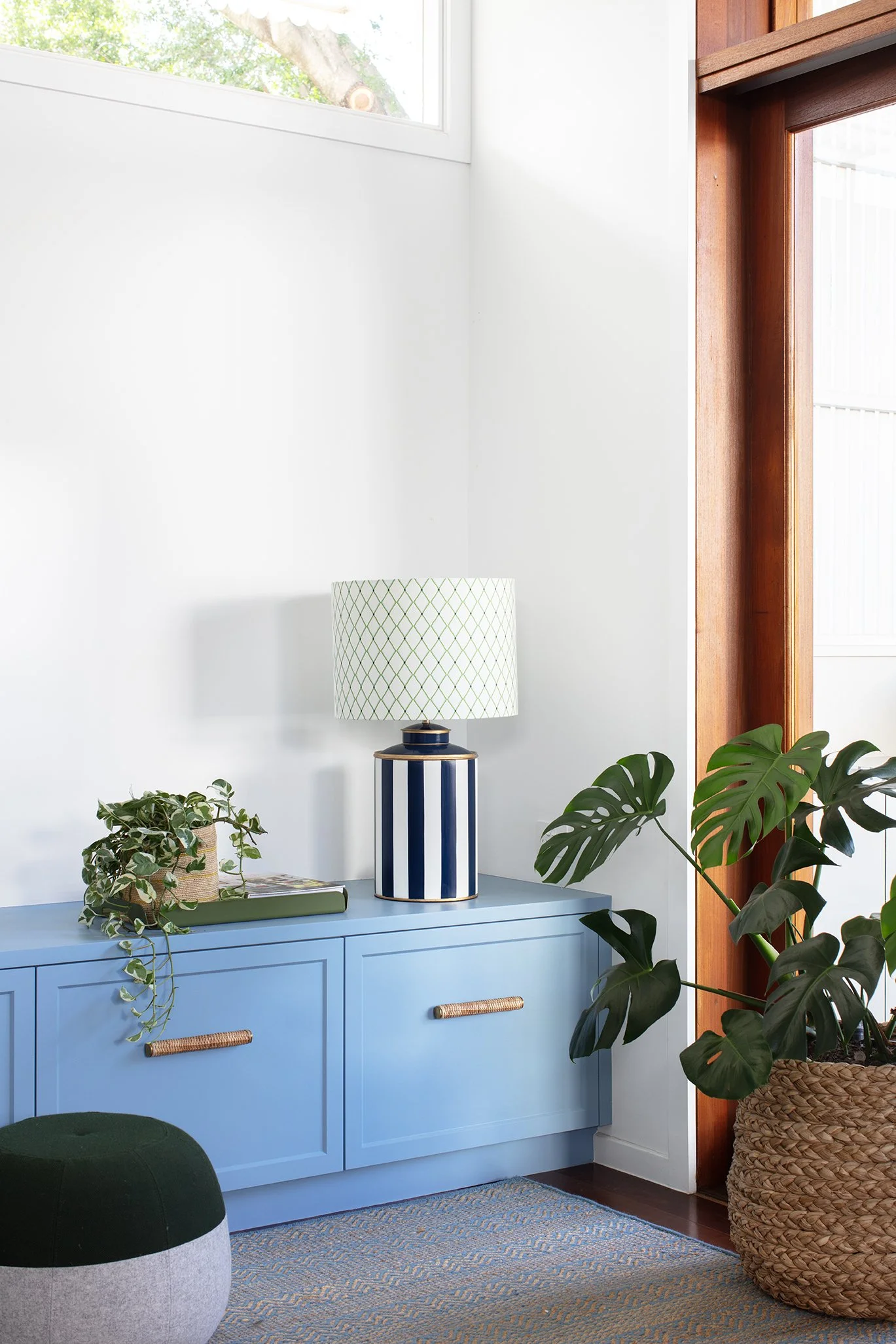 Playroom TV room featuring pretty blue cabinetry with rattan handles, a fun lamp, greenery, and a cute ottoman blending greens and blues
