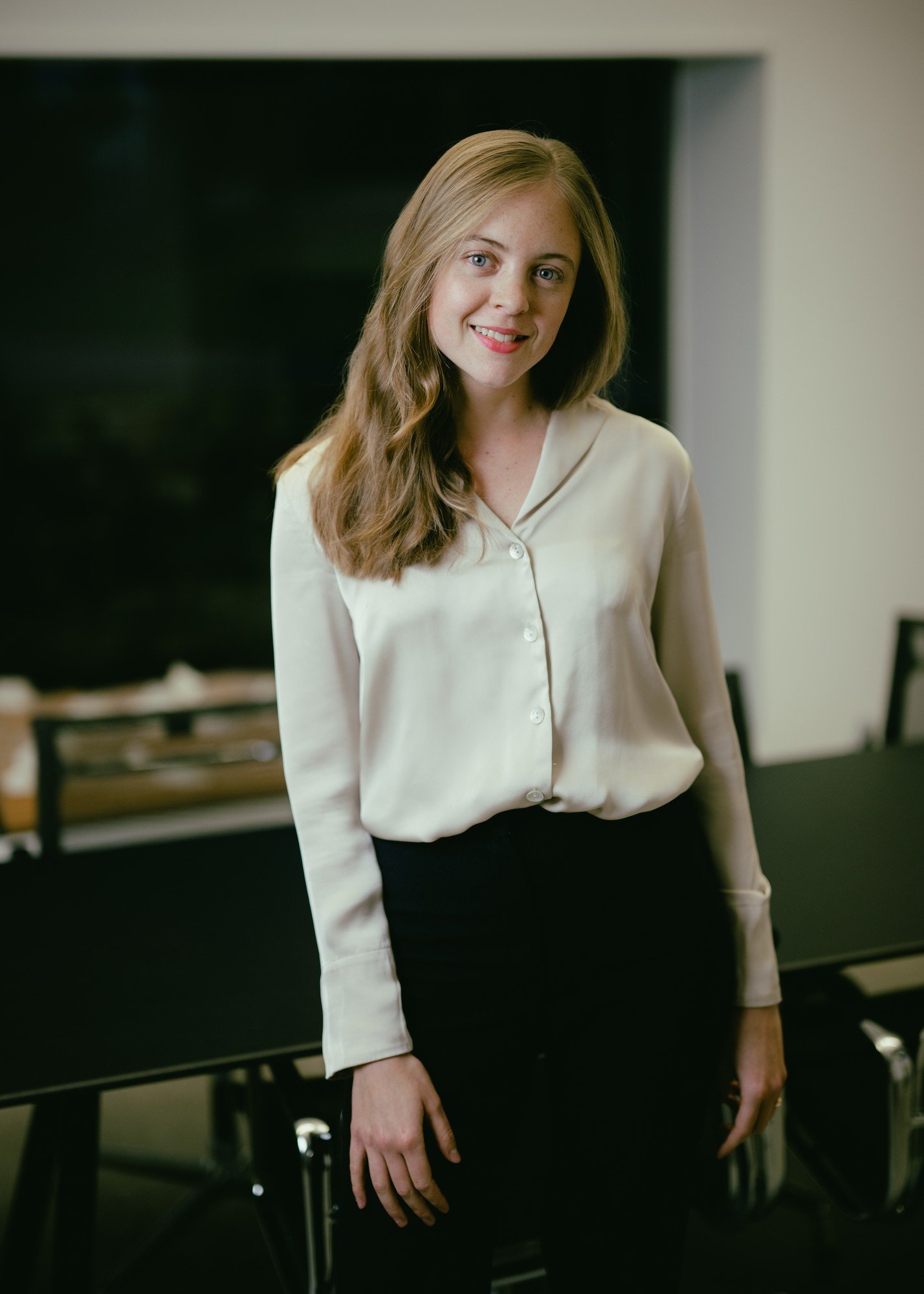 Eine junge Frau in weisser Bluse steht vor einem schwarzen Tisch und lächelt in die Kamera.