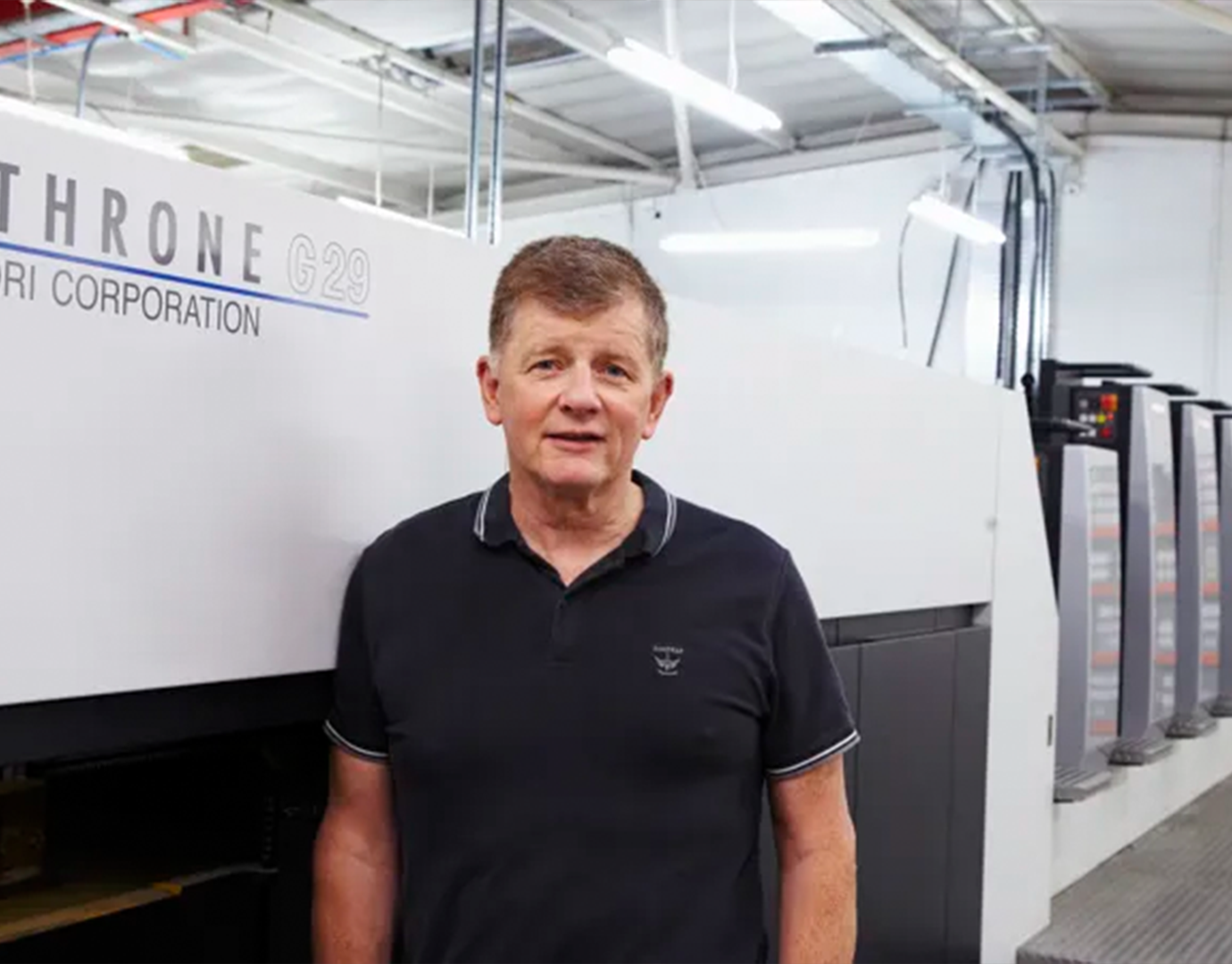 Man standing next to a large printing machine in an industrial setting