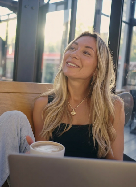 A woman named Ellyn Hunt with long blonde hair smiling while sitting in a cafe with sunlight coming through large windows.