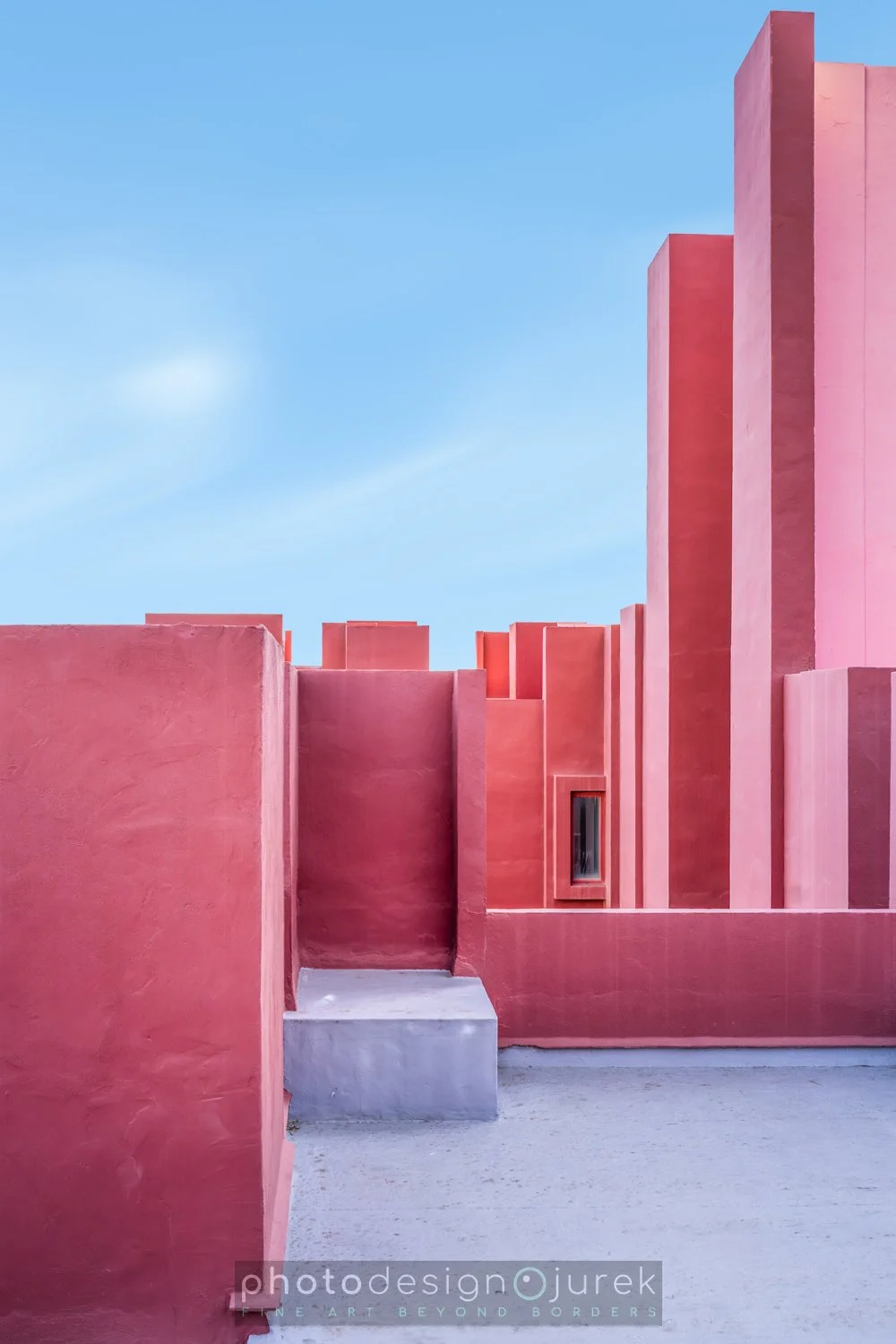 Colorful pink and red architectural structures with a small window, set against a clear blue sky.