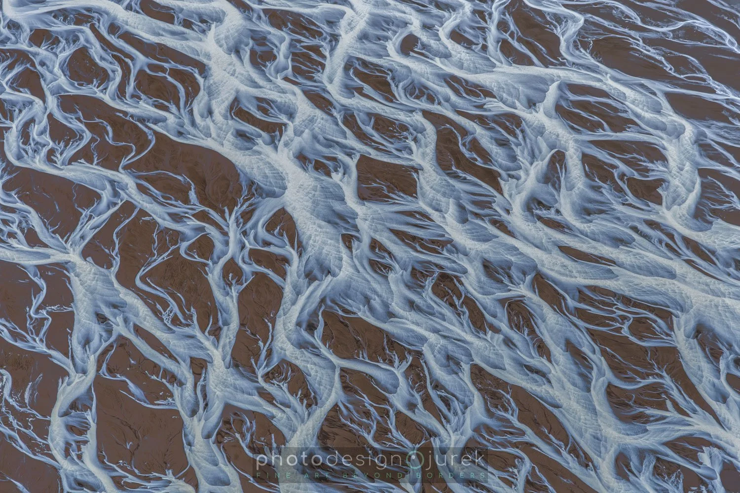 Aerial view of ocean waves washing over sandy beach, creating intricate white foam patterns.
