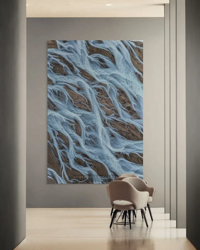 An interior space with a large abstract painting of flowing water or ice on the wall, and a small seating area with a single beige armchair and three small black-legged stools.