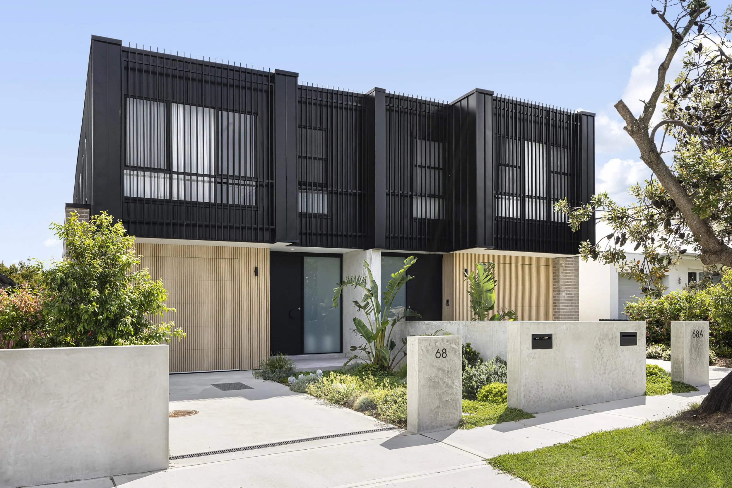 Modern two-story duplex house with black exterior, wooden accents, and greenery in front.