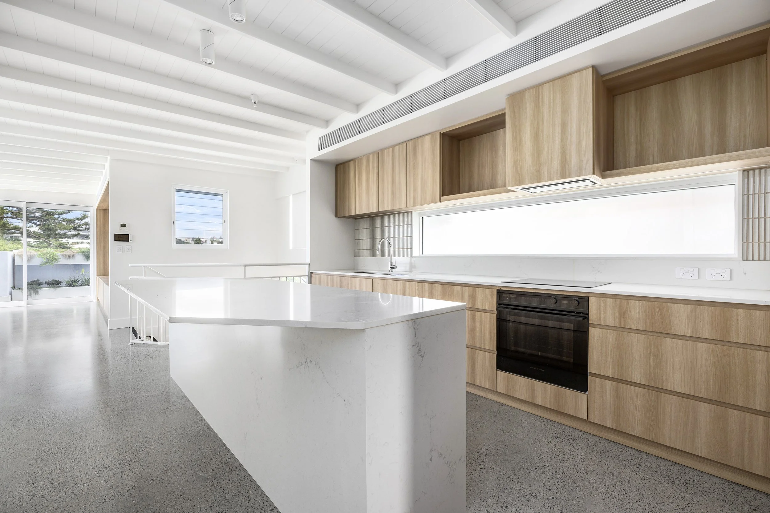 Modern kitchen with white countertops, wooden cabinets, and large windows, bright and minimalist design.