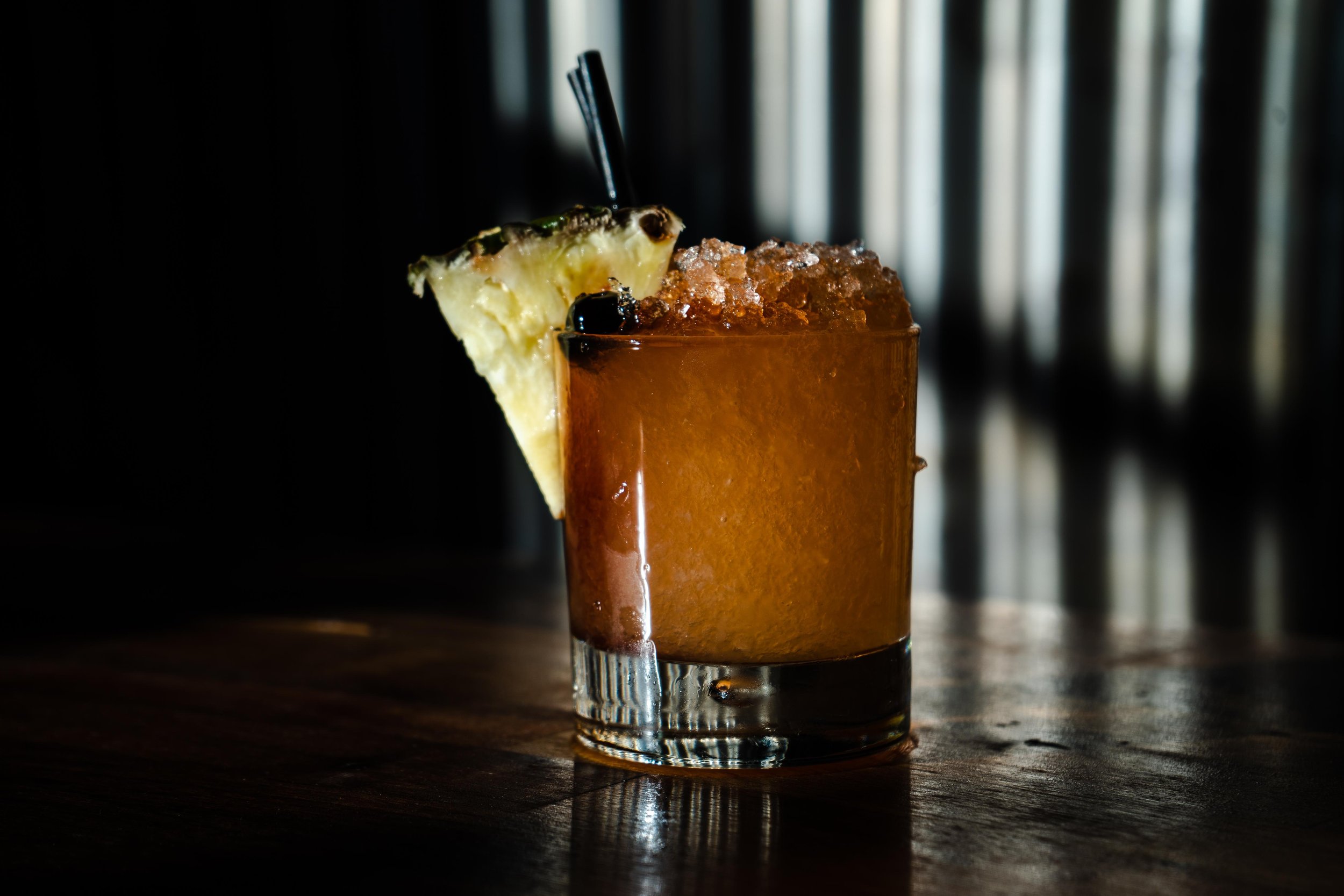 A cocktail in a short glass with crushed ice, garnished with a pineapple slice and a cherry.