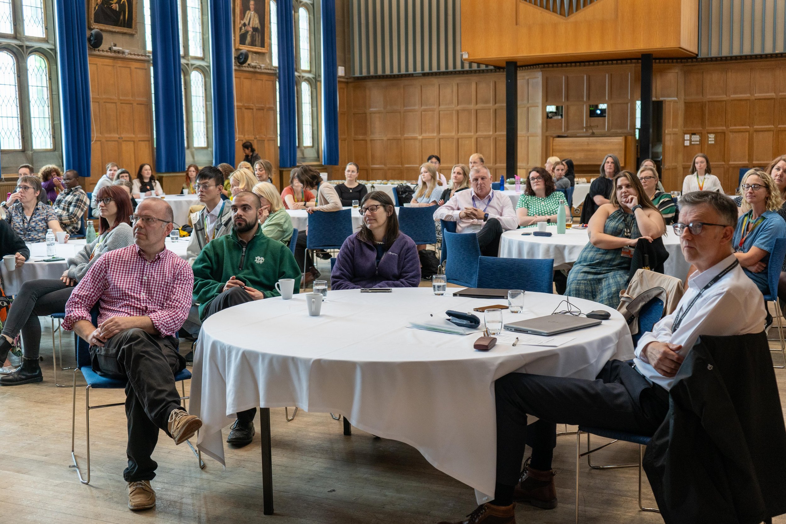 People sitting at round tables in a conference room, attentively listening to a presentation.
