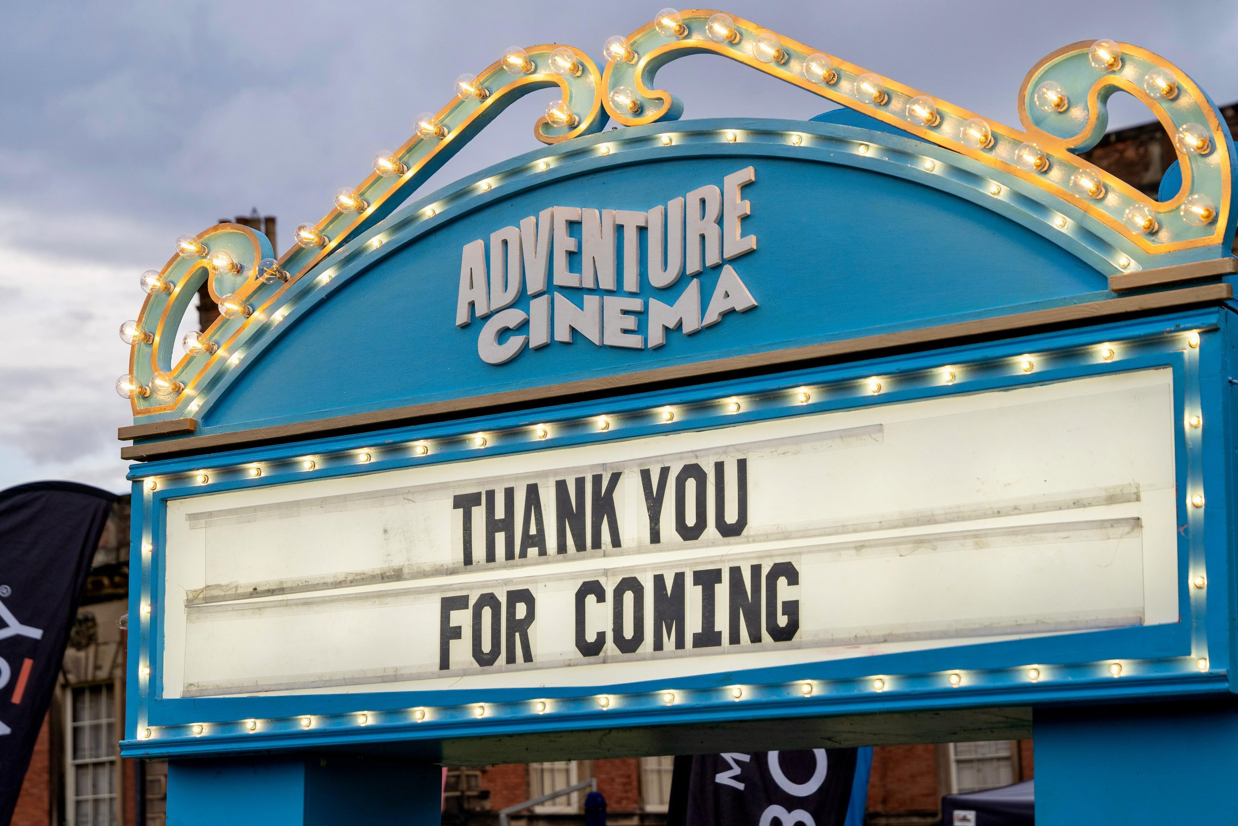 Blue and yellow illuminated cinema sign reading "Adventure Cinema" with the message "Thank You for Coming."
