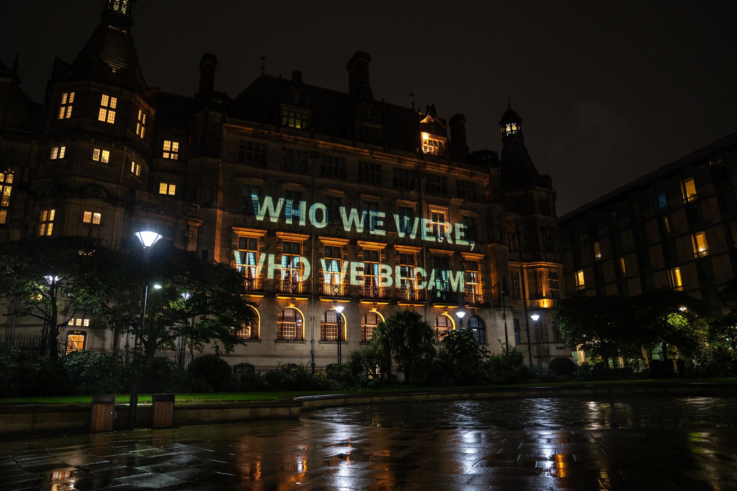 Historic building at night with projection reading 'WHO WE WERE, WHO WE BECAME.'