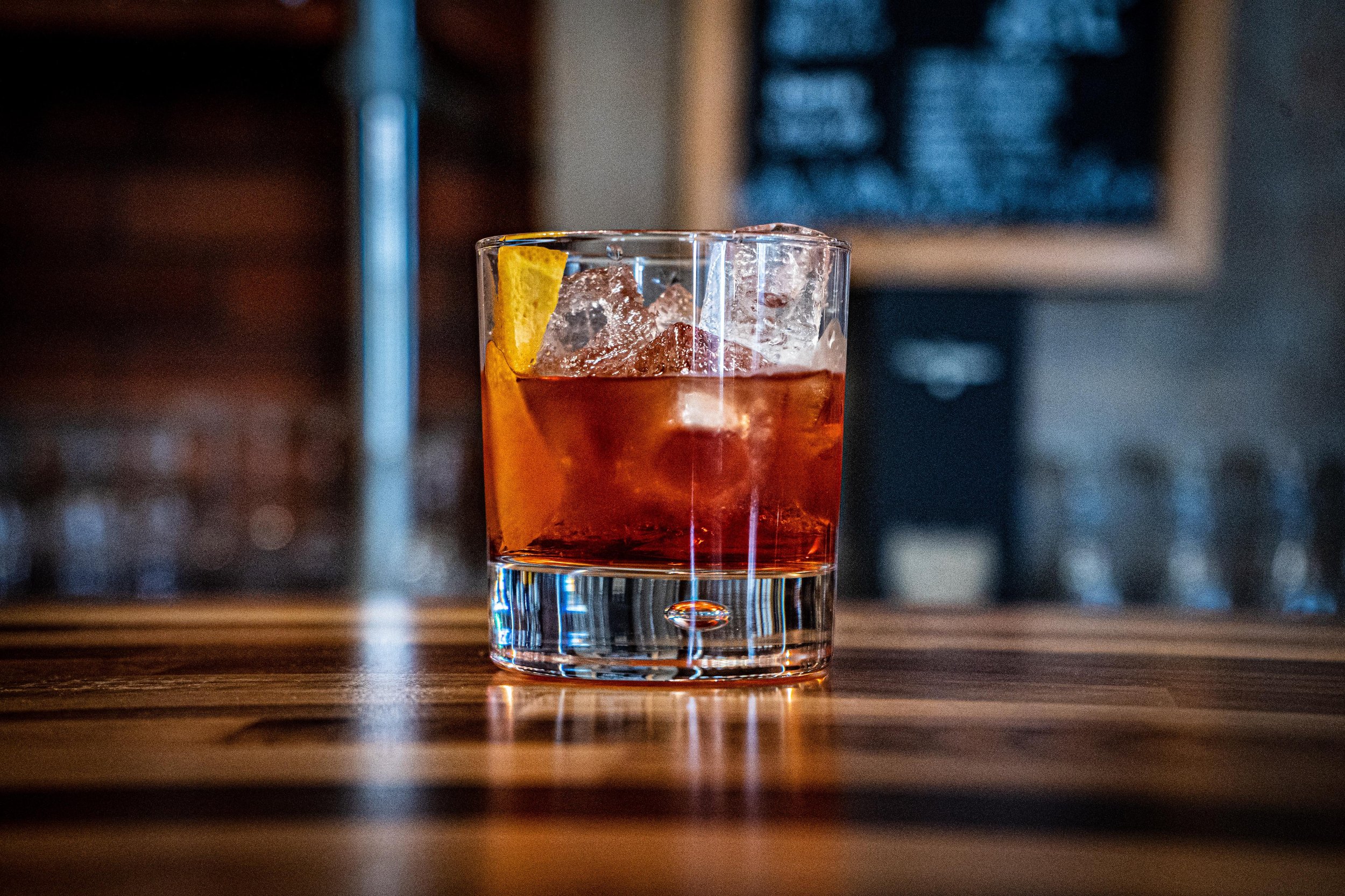 Glass of Negroni cocktail with ice and orange peel on wooden bar