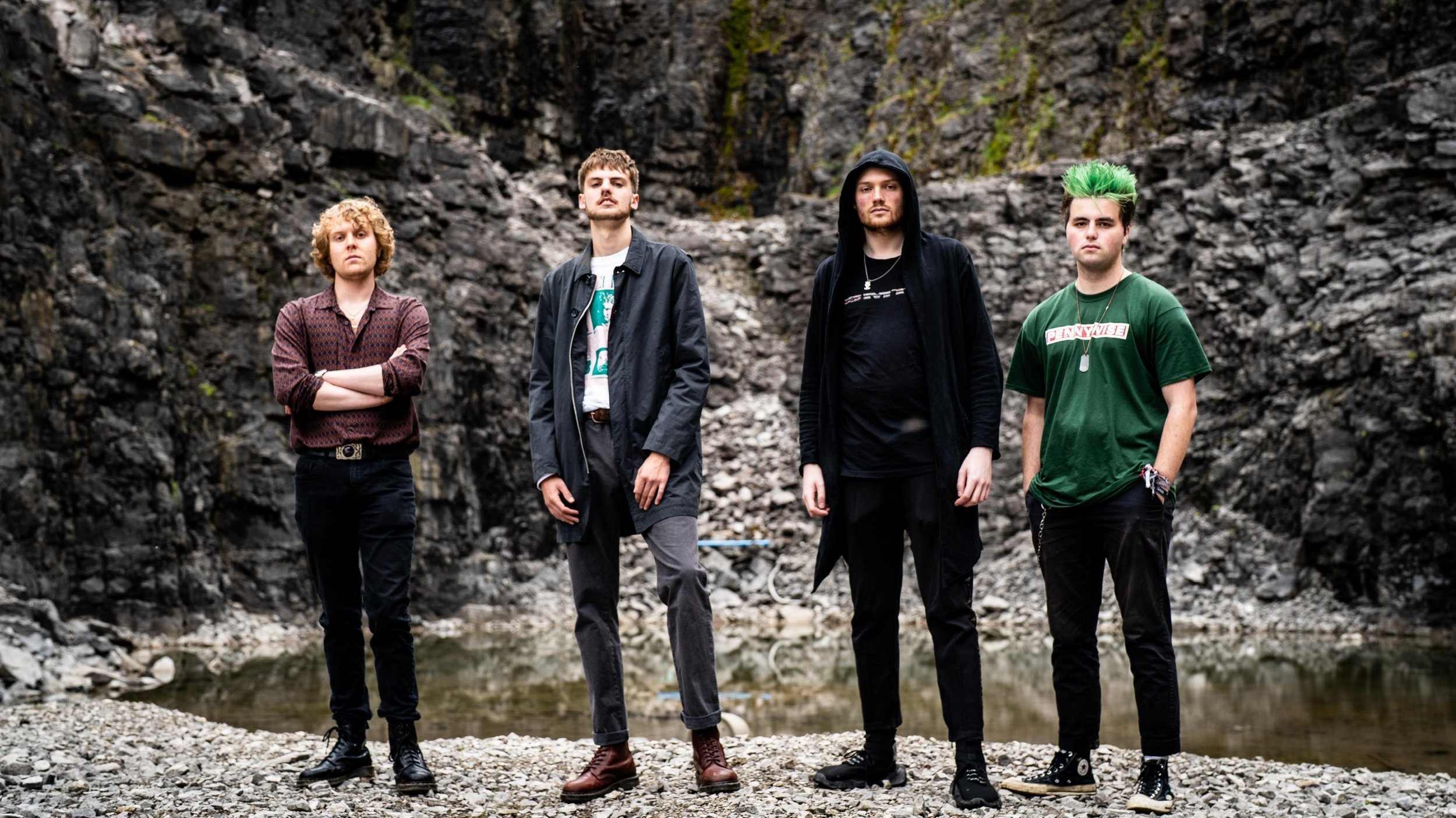 Four men standing outdoors against a rocky background.