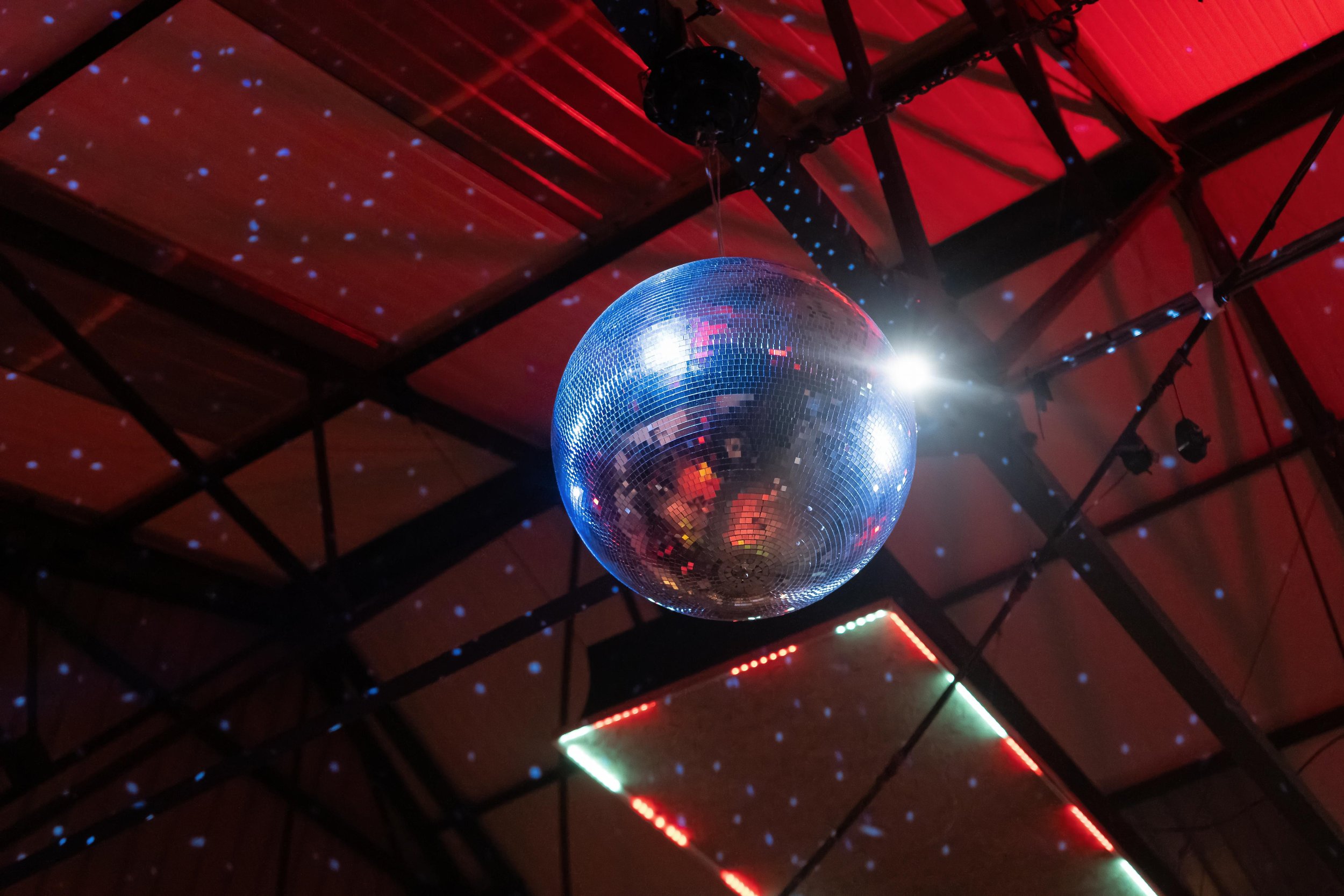 Disco ball hanging from ceiling with red panels and light reflections.