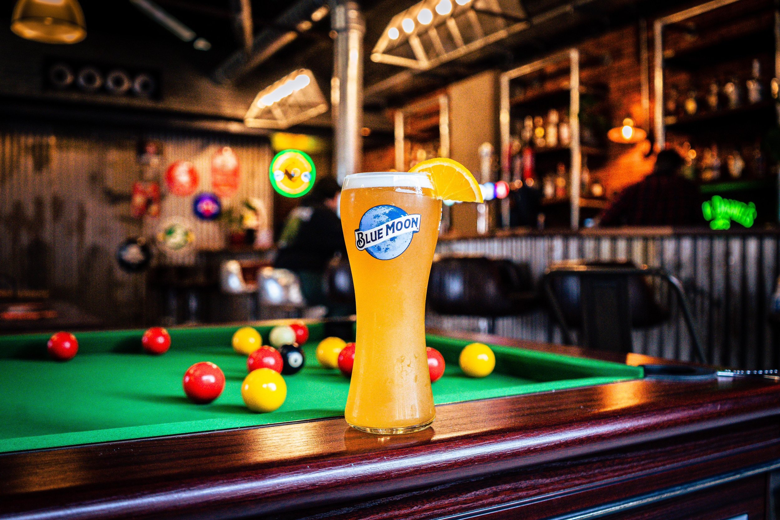 Glass of Blue Moon beer with orange slice on pool table in a bar setting