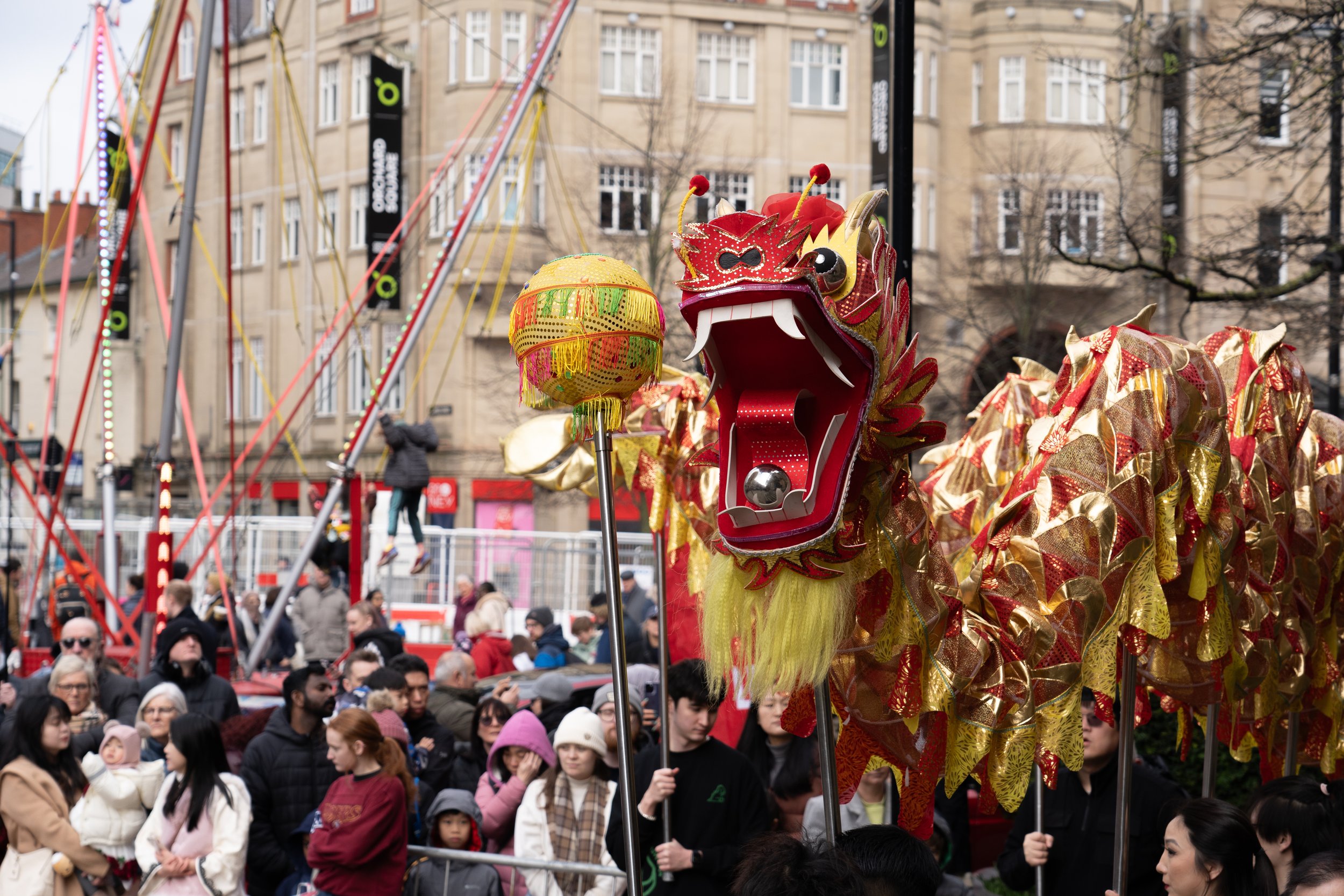 A lively parade featuring a colorful Chinese dragon puppet held by multiple performers in front of an audience on a city street.