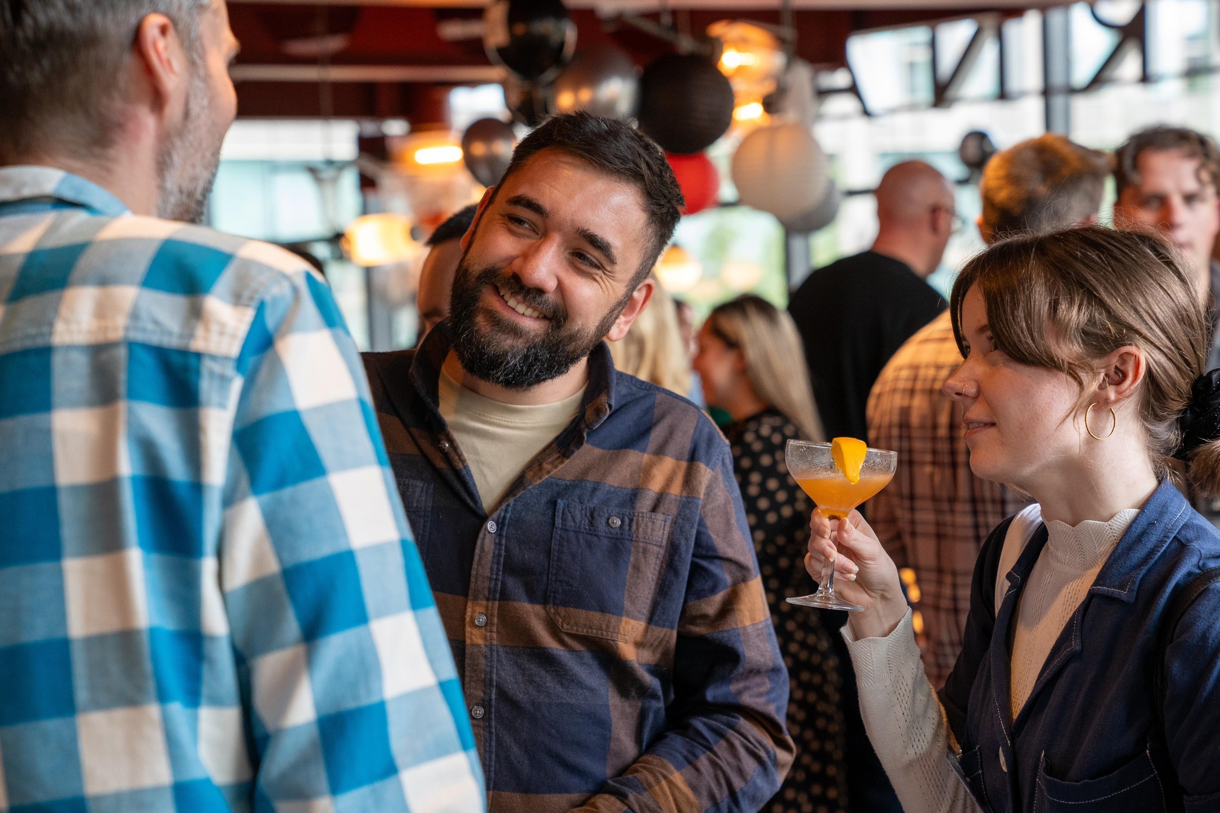 People socializing at a party, a woman holding a cocktail glass with an orange slice.