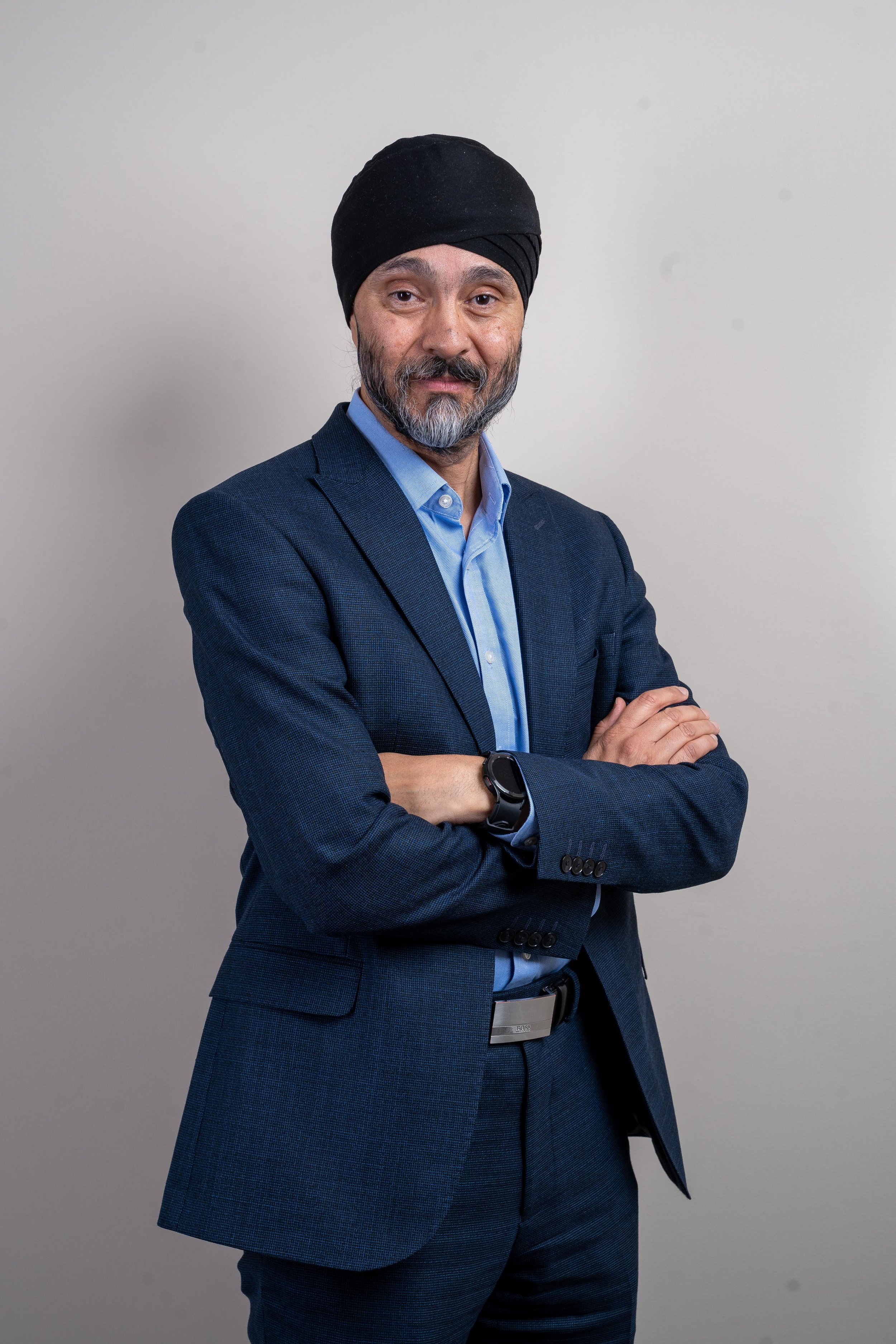 Man in blue suit wearing a turban, arms crossed, neutral background.