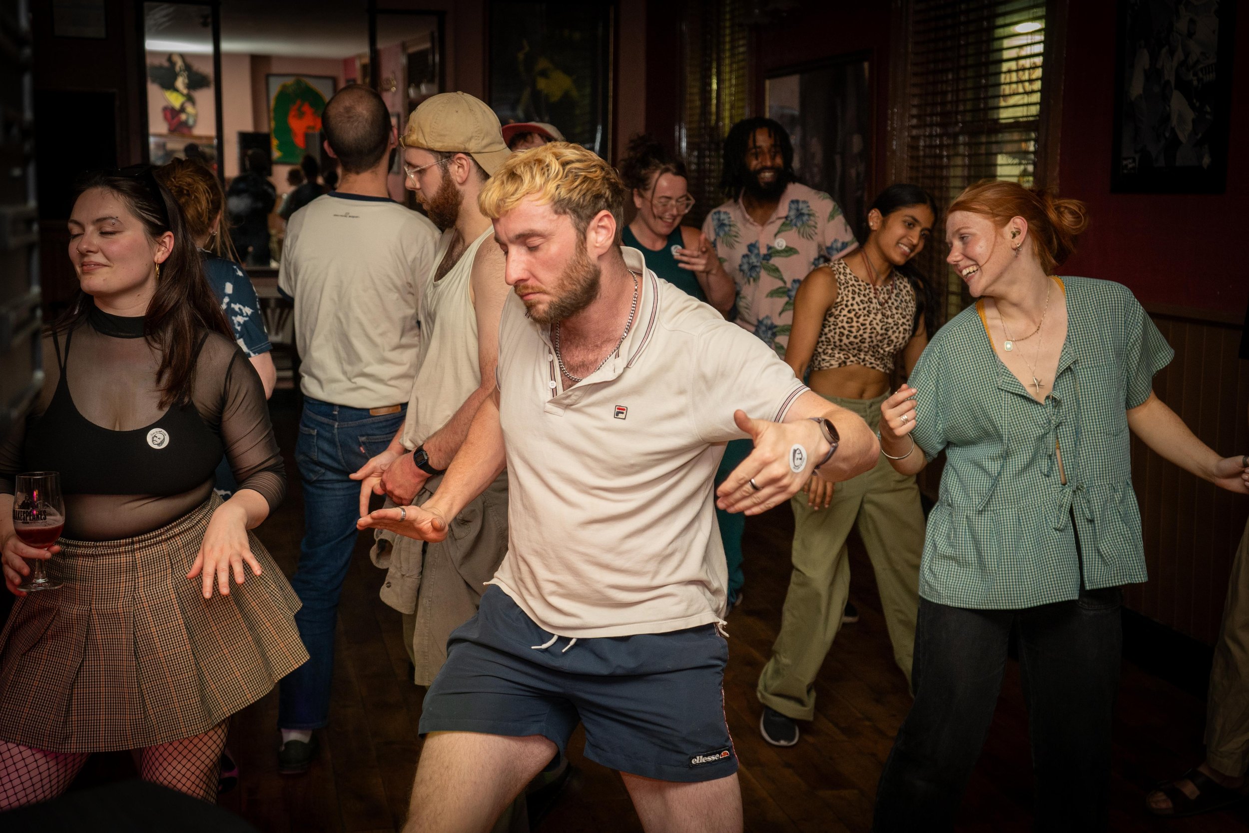 People dancing at a party or social gathering in a dimly lit room with wooden floors.