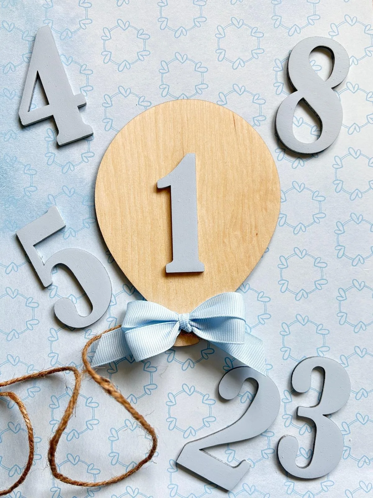 Numeri in rilievo di colore bianco e una croce di tessuto azzurro, con uno sfondo decorato con cuori.