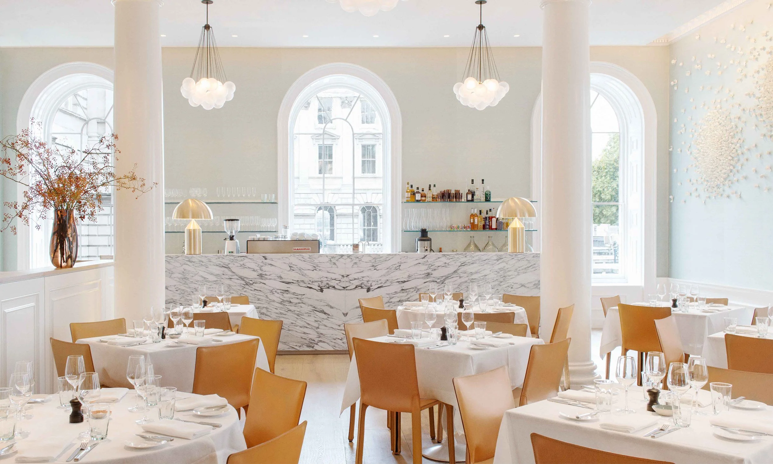 Spring at Somerset House with white tablecloths, brown chairs, marble bar, and large windows.