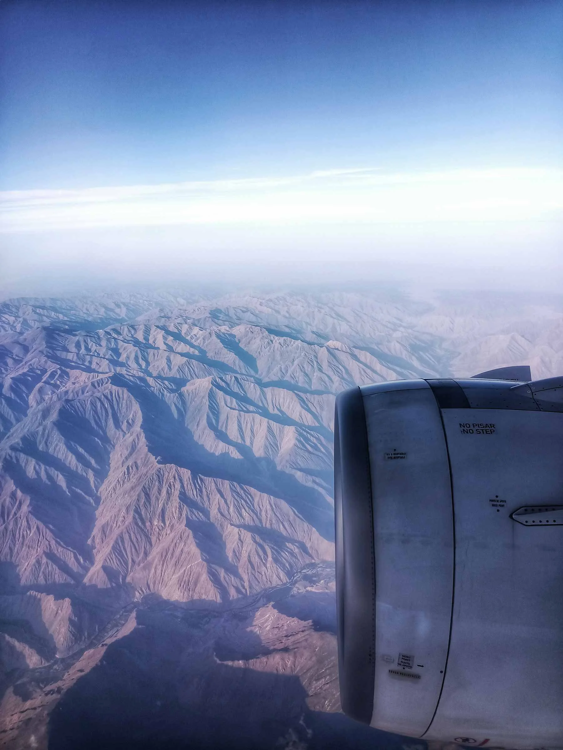 Vue depuis un avion montrant une chaîne de montagnes enneigées en dessous et une partie du moteur de l'avion à droite, avec un ciel clair au-dessus.