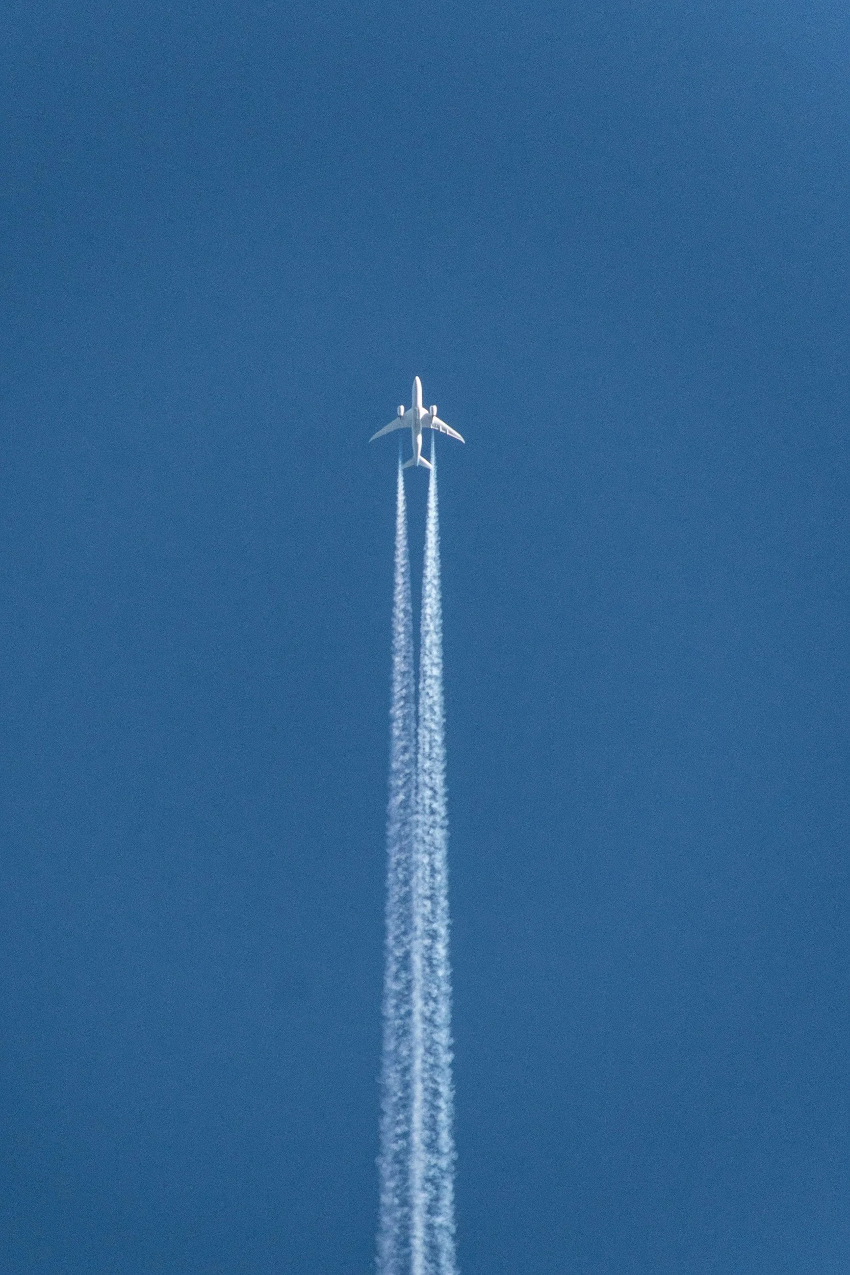 Un avion de ligne en vol haut dans le ciel, laissant derrière lui deux traînées de condensation.