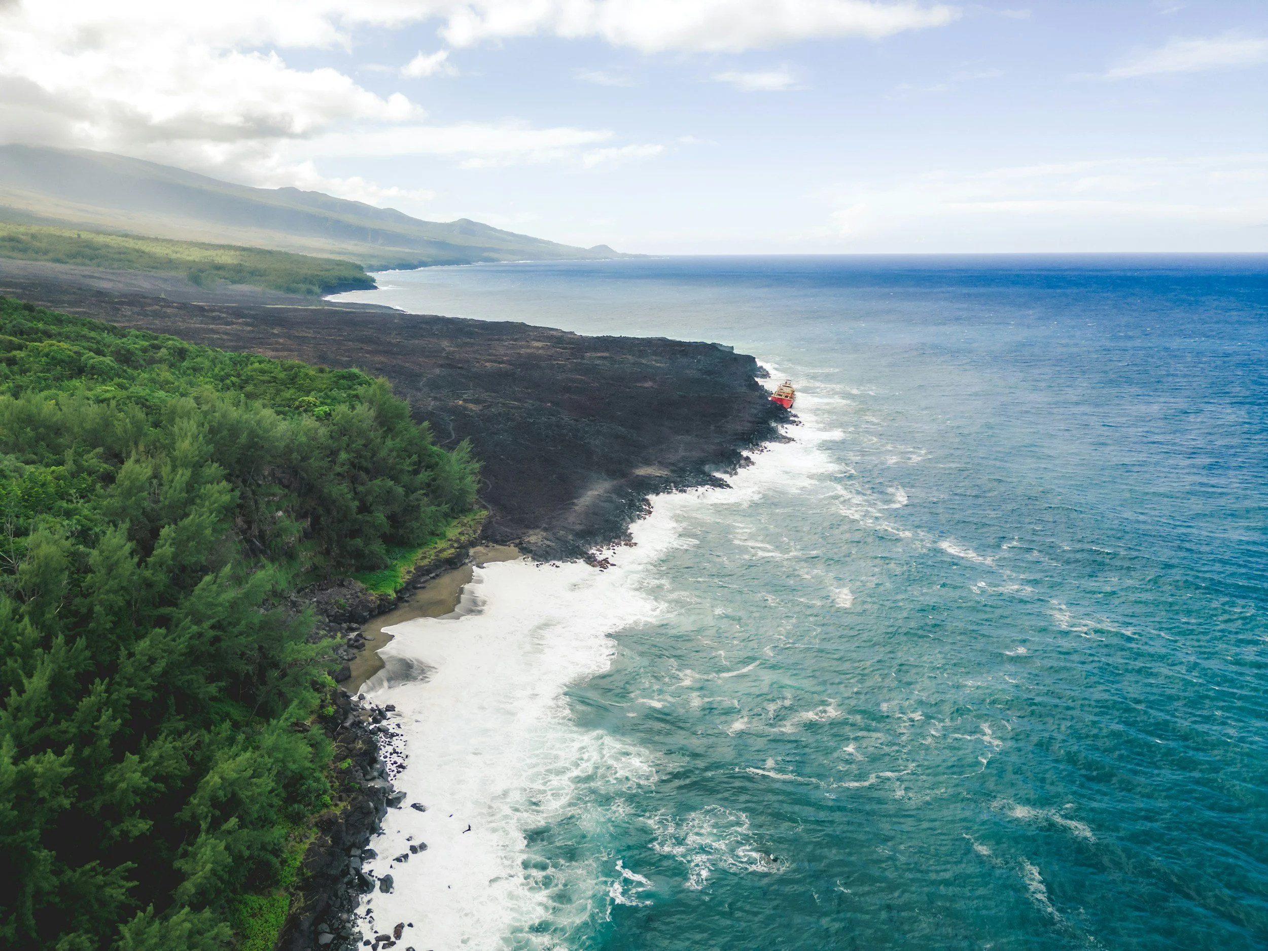 Côte rocheuse avec végétation verte, mer avec vagues, et un bateau rouge au loin