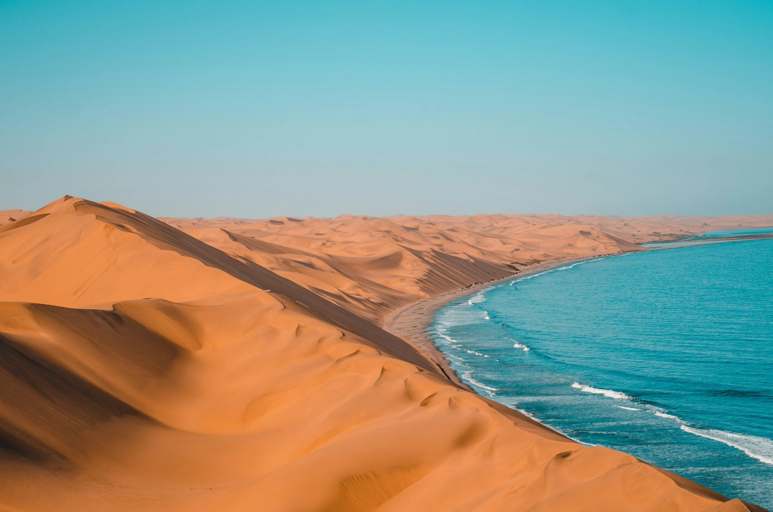 Dunes de sable doré le long d'une côte avec mer bleue calme et ciel clair.