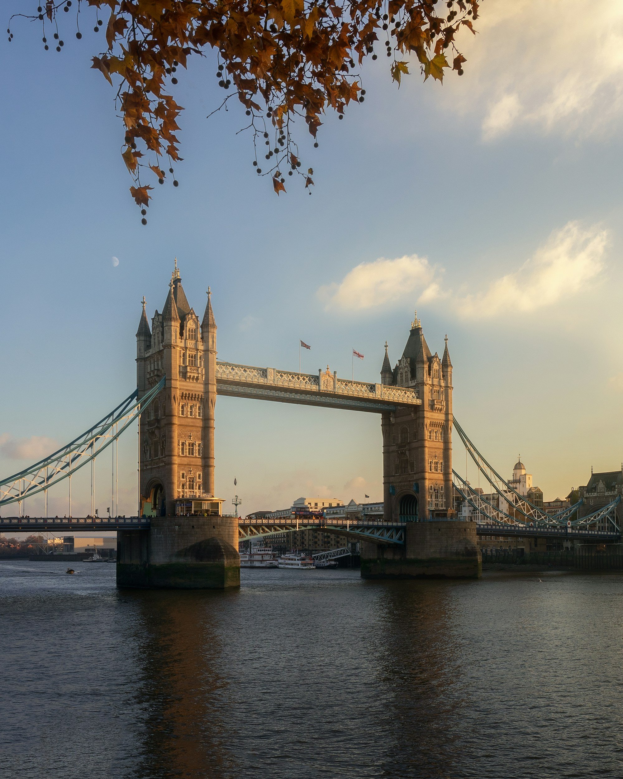 Le pont de Londres, célèbre monument avec ses deux tours gothiques, au bord de la rivière, sous un ciel clair avec quelques nuages et la lune visible.