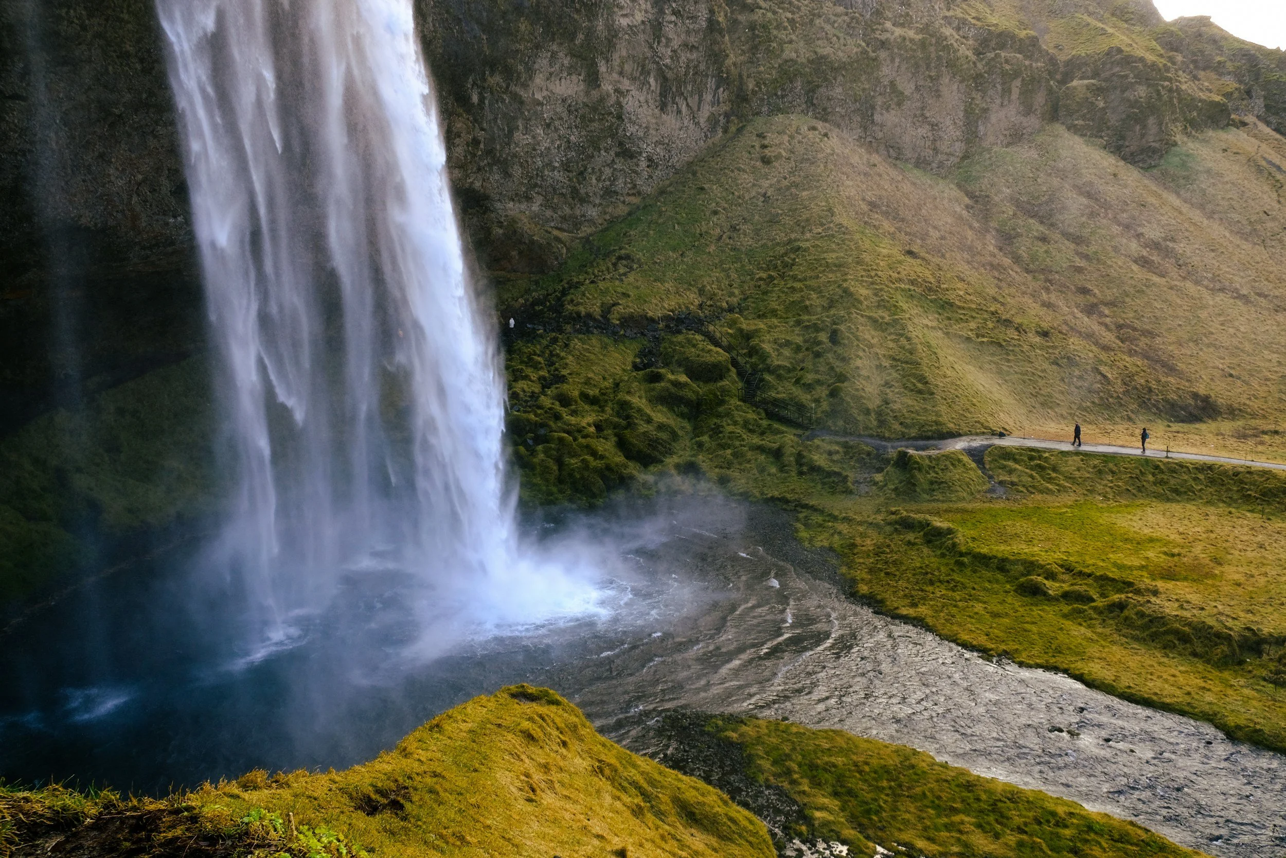Cascade d'eau dans un paysage verdoyant avec deux personnes marchant le long d'un sentier.