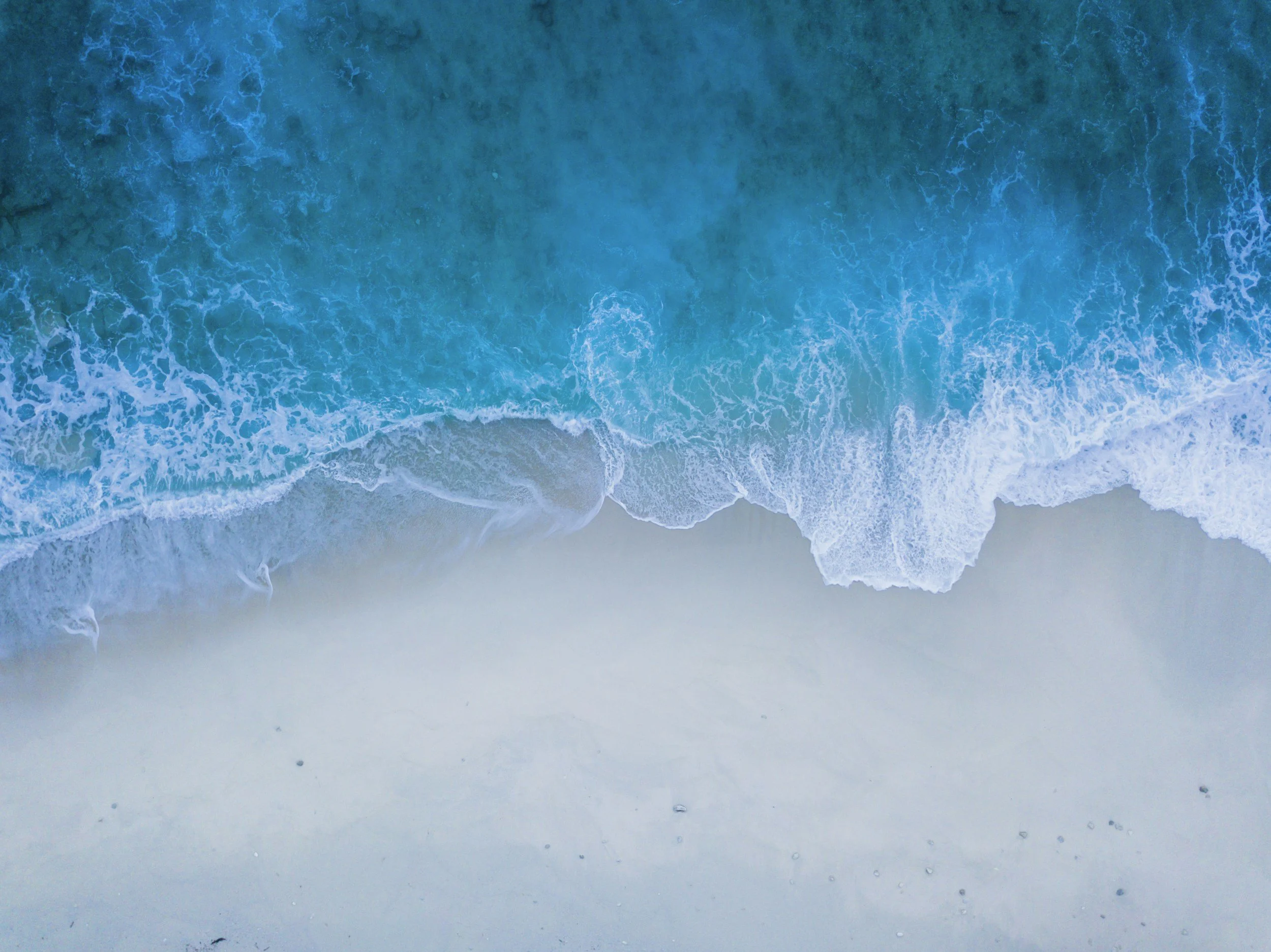 Vue aérienne d'une plage avec des vagues bleues s'écrasant sur le sable blanc.