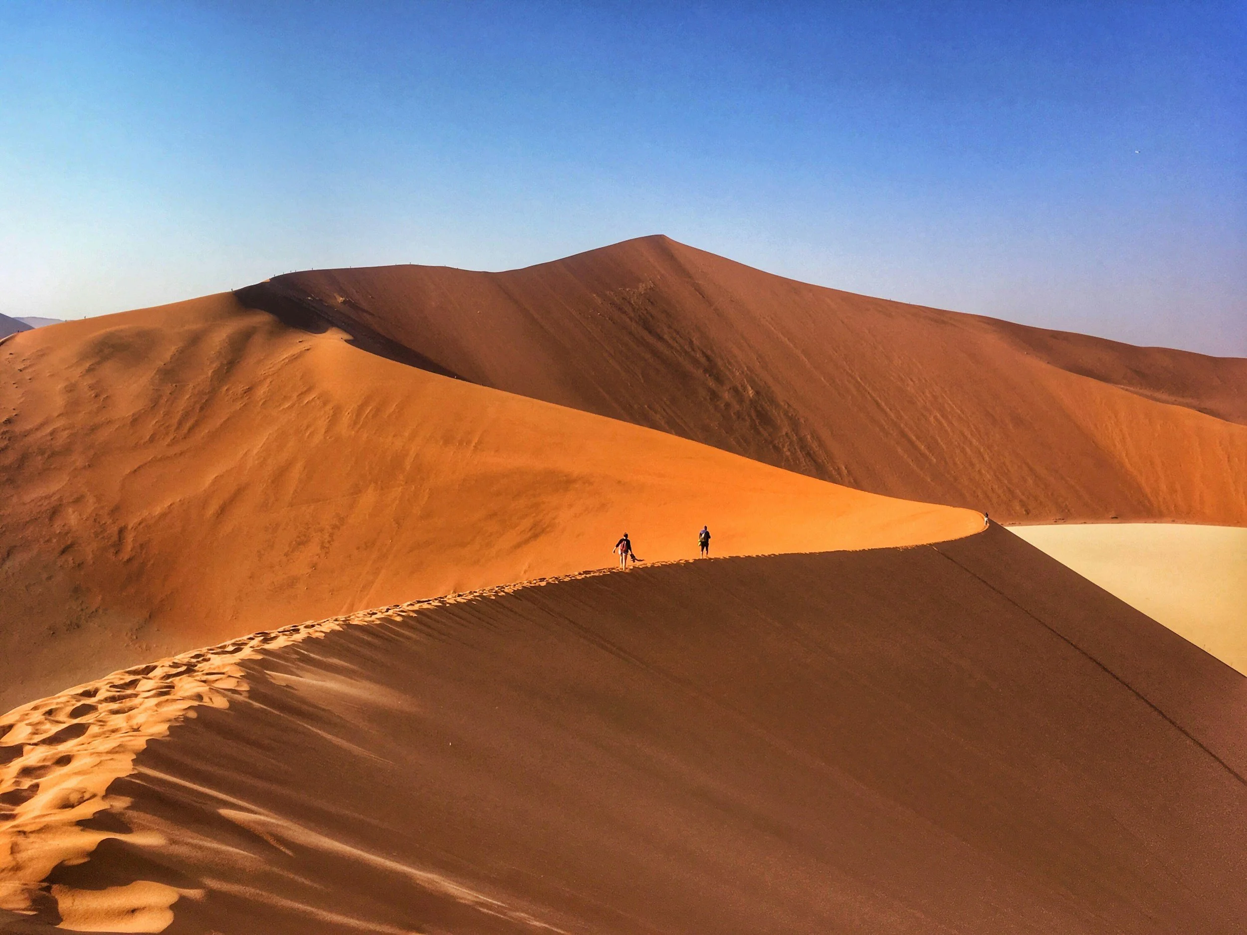 Deux personnes marchent sur la dune d'une grande chaîne de dunes de sable dans un désert au coucher du soleil ou à l'aube.