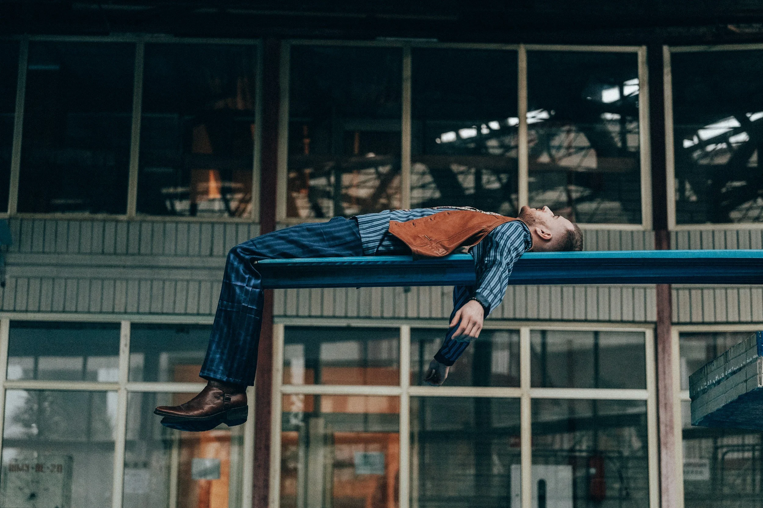 Un homme allongé sur une table, corps suspendu dans un bâtiment industriel.