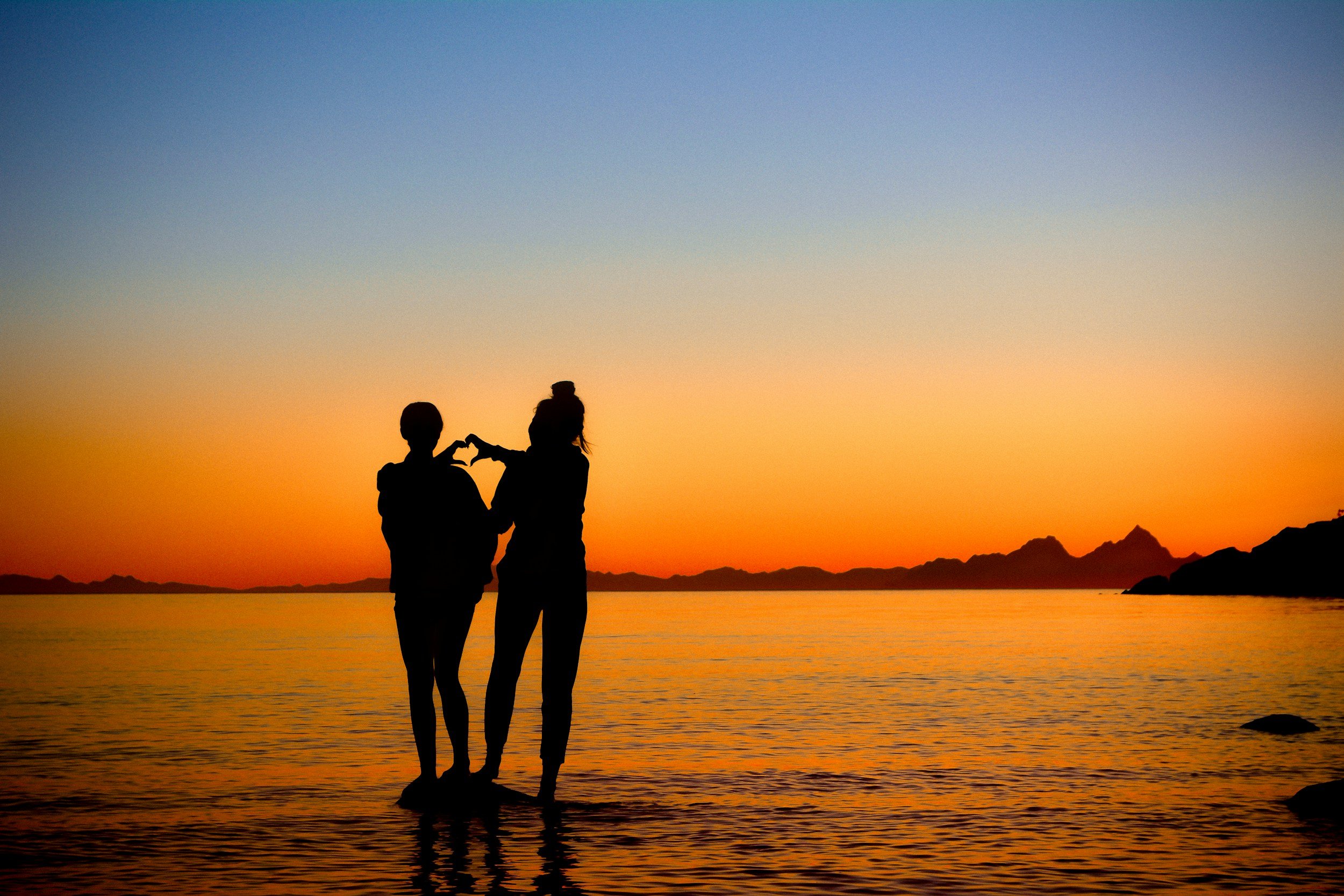 Une femme marche dans un désert de sable en regardant un coucher de soleil ou un lever, avec un ciel bleu clair et la lune visible dans le ciel.