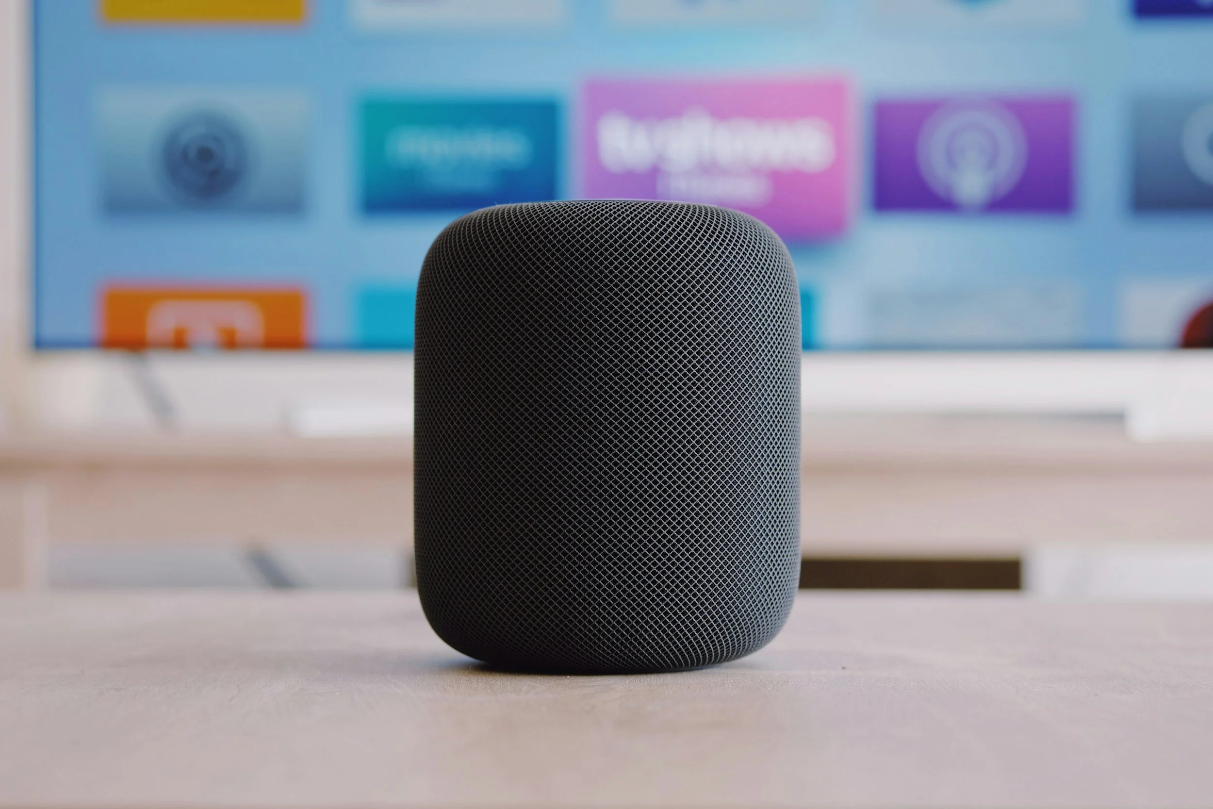 enceinte intelligente noire sur une table en face d'un écran d'ordinateur