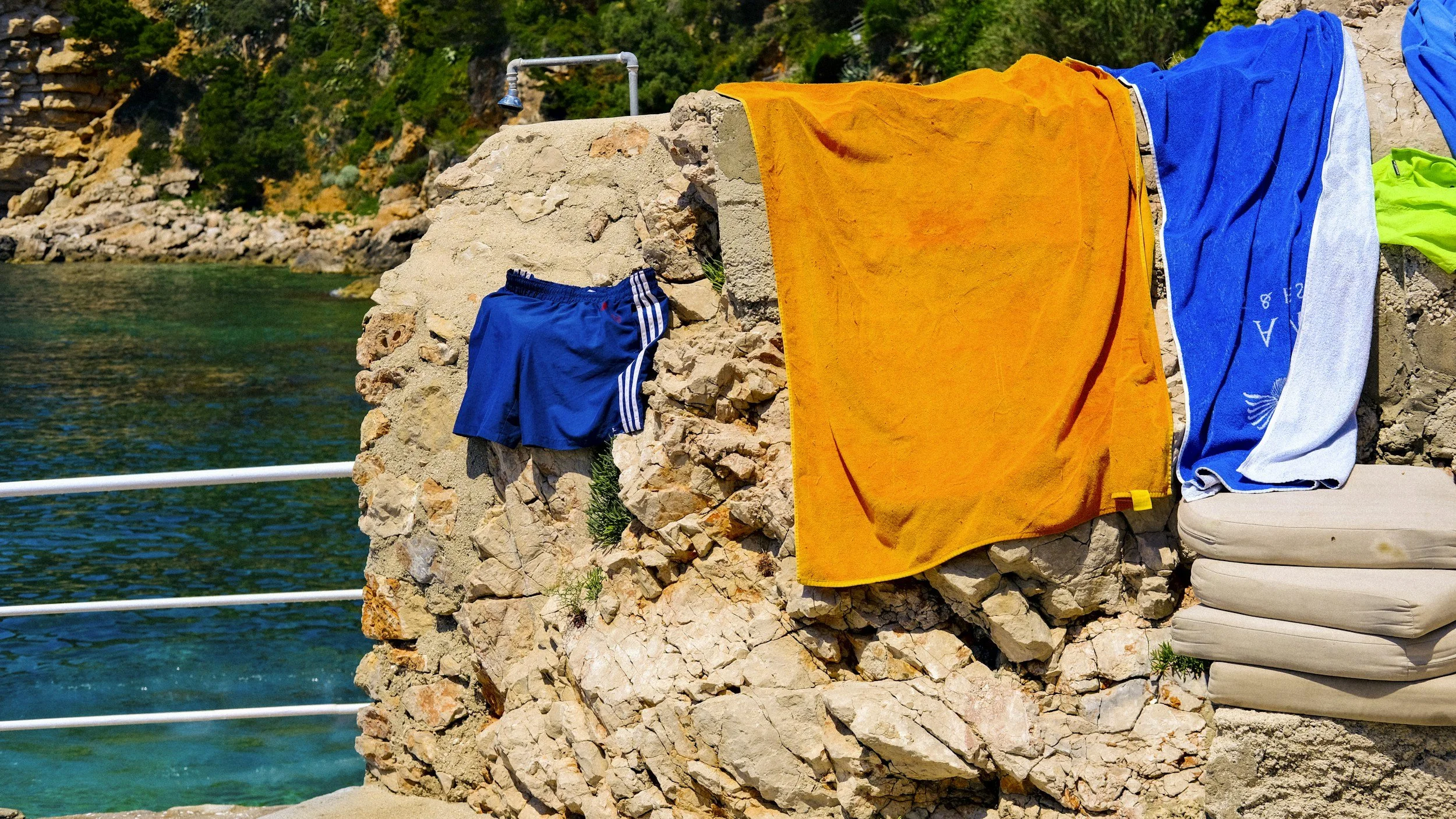 Vêtements ou serviettes suspendus pour sécher, suspendus sur une paroi rocheuse au bord de l'eau, avec des montagnes en arrière-plan.