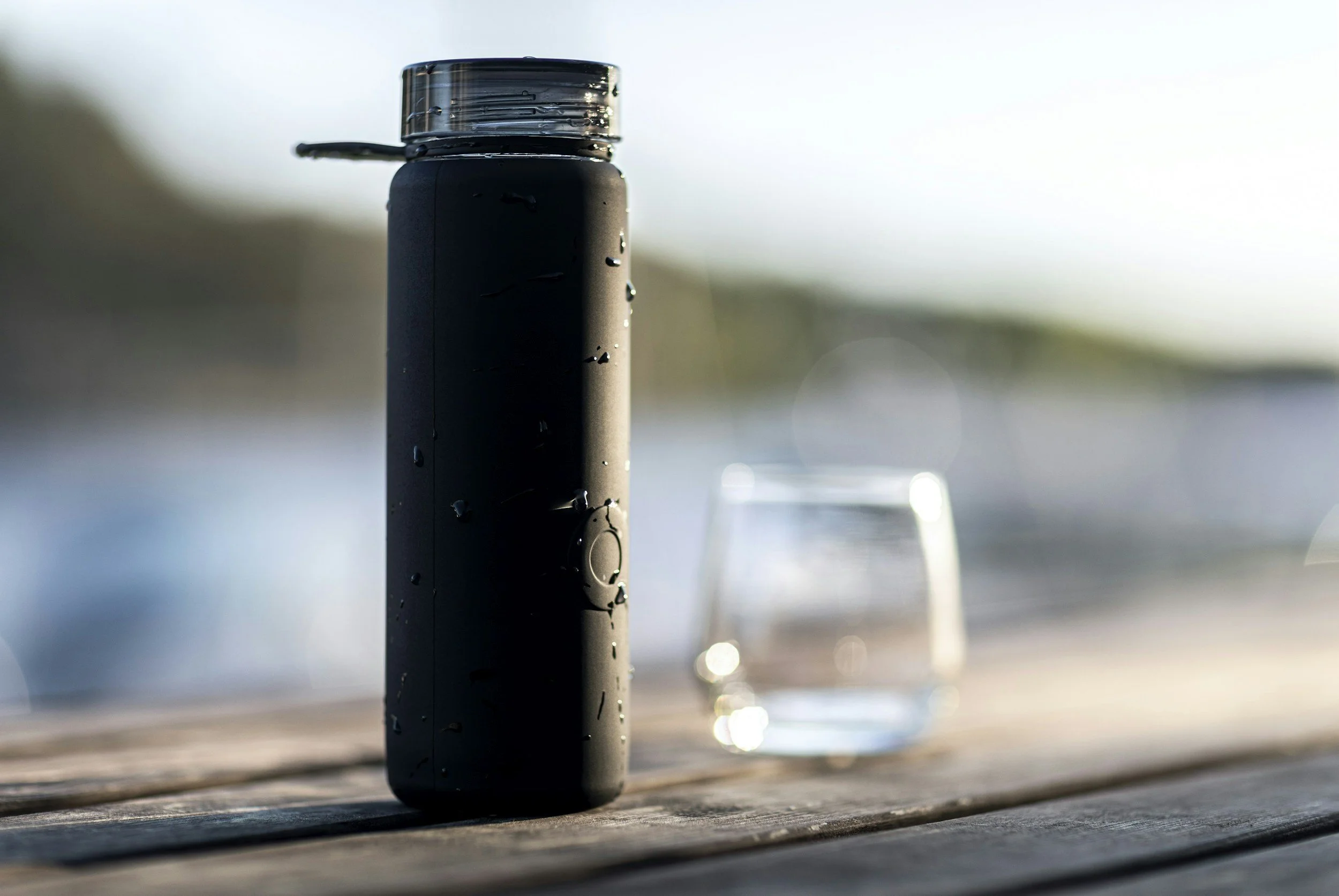Un diffuseur noir avec un couvercle transparent, à côté d'un verre d'eau sur une surface en bois.