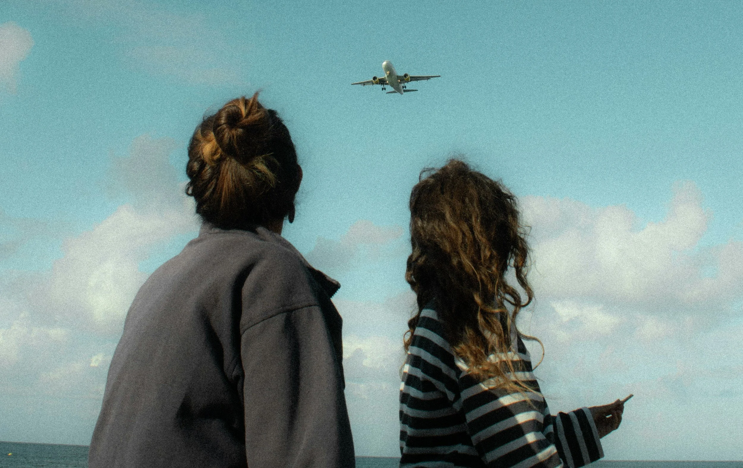 Deux femmes regardant un avion qui vole dans le ciel au-dessus de la mer.