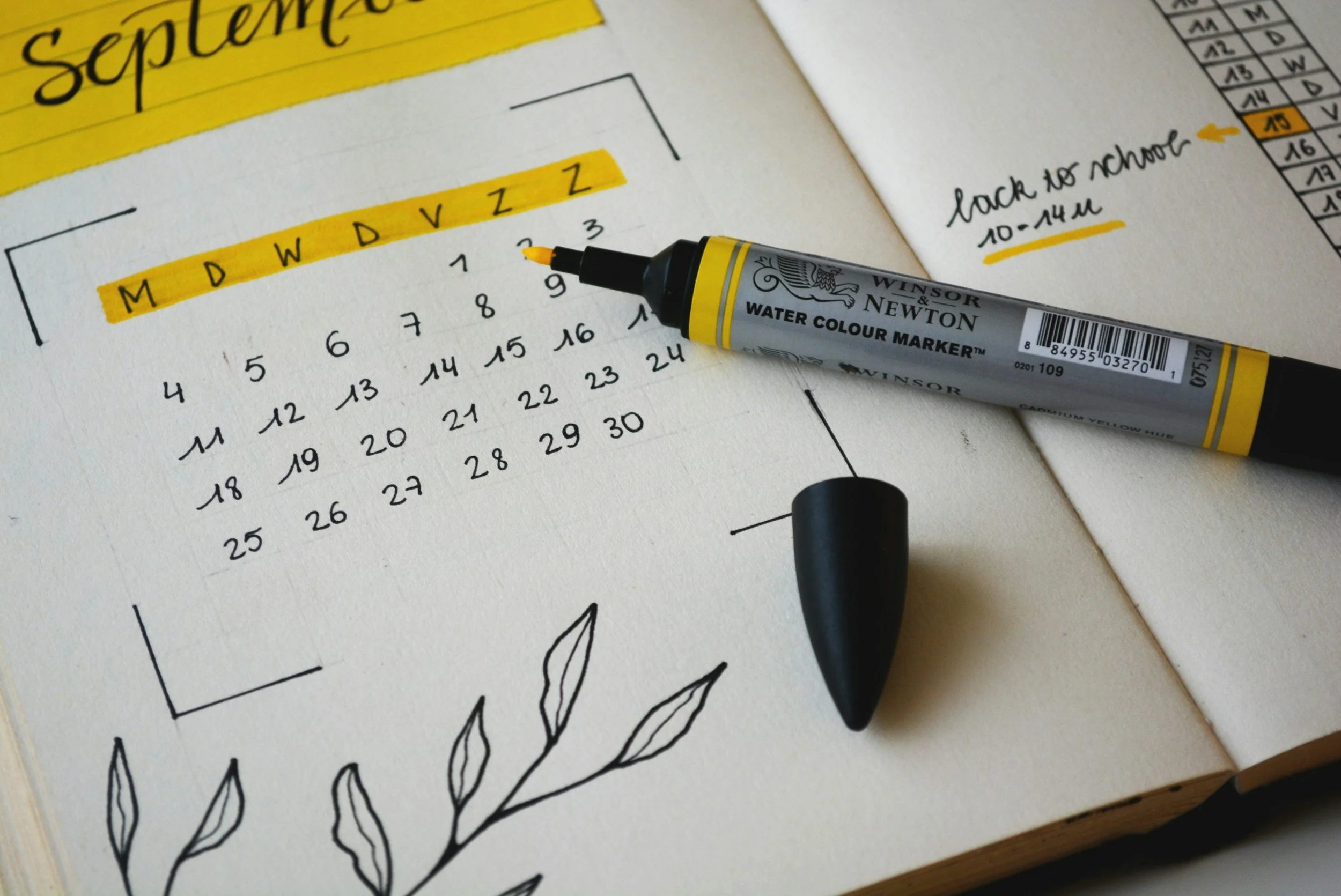 Page d'agenda ou calendrier avec le mois de septembre, texte en français, stylé avec une surbrillance jaune, une marque-water de couleur jaune gris et une illustration de branches avec des feuilles noires, un stylo et un marqueur dans le carnet.