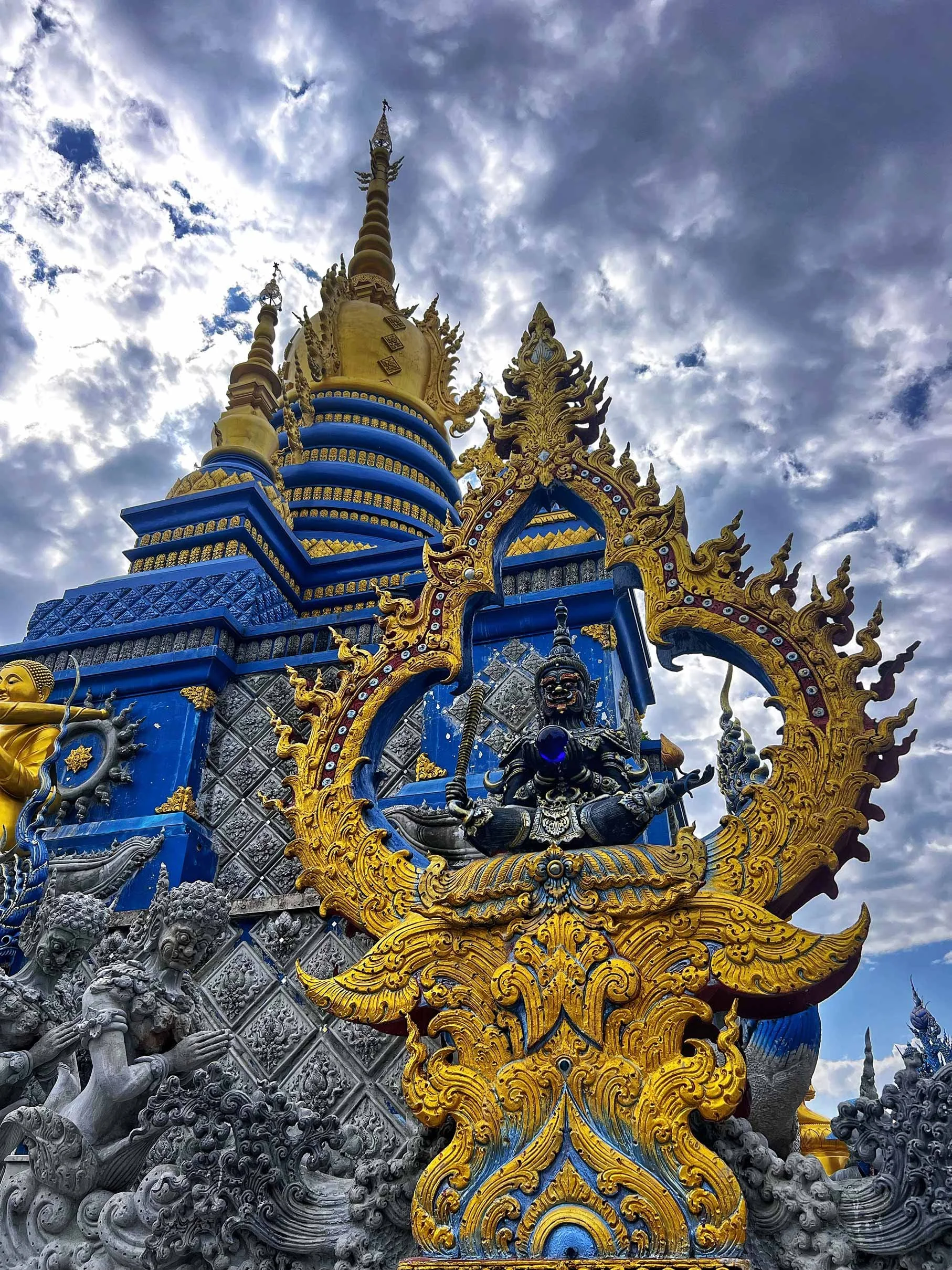 Un temple coloré avec une structure dorée, des statues, et un ciel nuageux en arrière-plan.