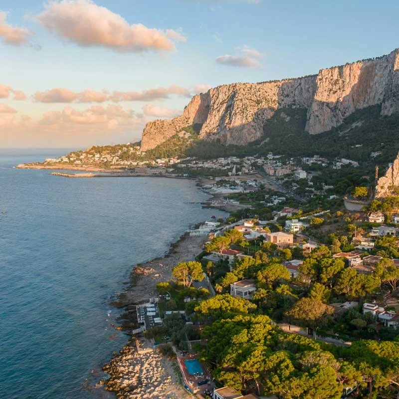 Paysage côtier avec des maisons, des arbres verts et des montagnes en arrière-plan au coucher du soleil