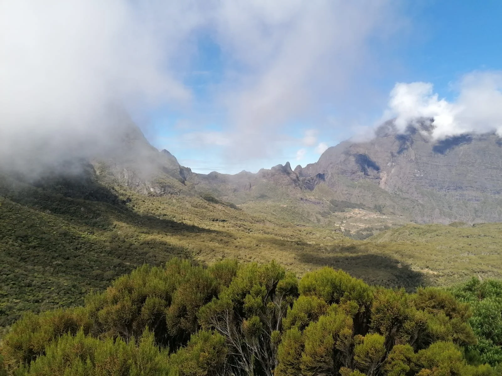 Vue de montagnes verdoyantes avec des nuages et un ciel partiellement bleu.