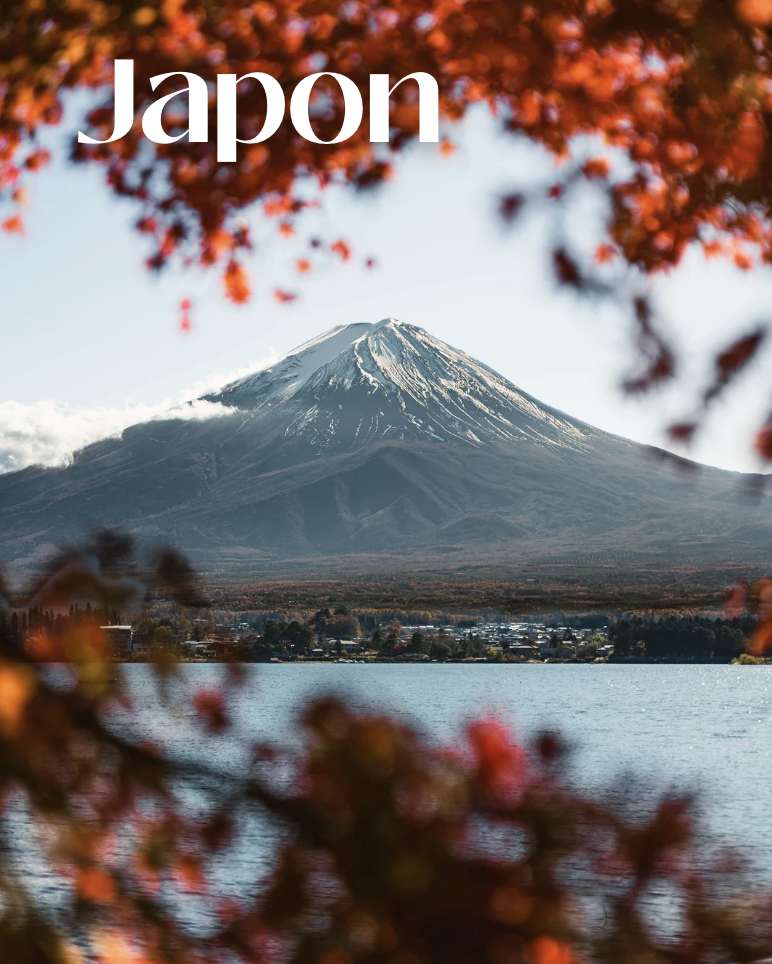 Le mont Fuji vu à travers des feuilles d'automne rouges et oranges, avec un lac au premier plan.