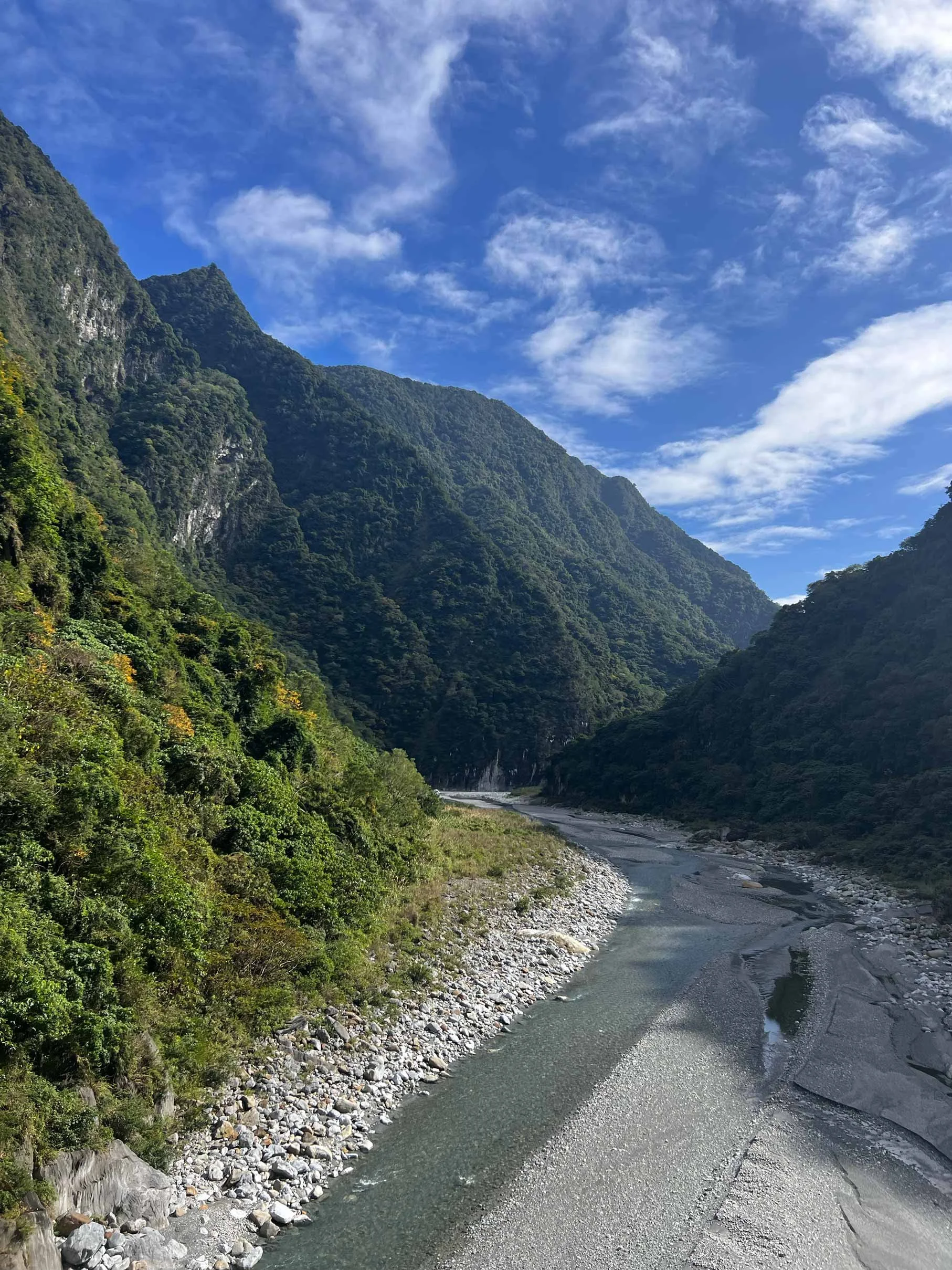 Vallée montagneuse avec rivière et paysage verdoyant sous un ciel bleu avec quelques nuages.