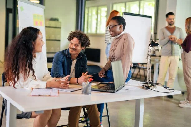 People having a discussion in a modern office with whiteboard and laptop.