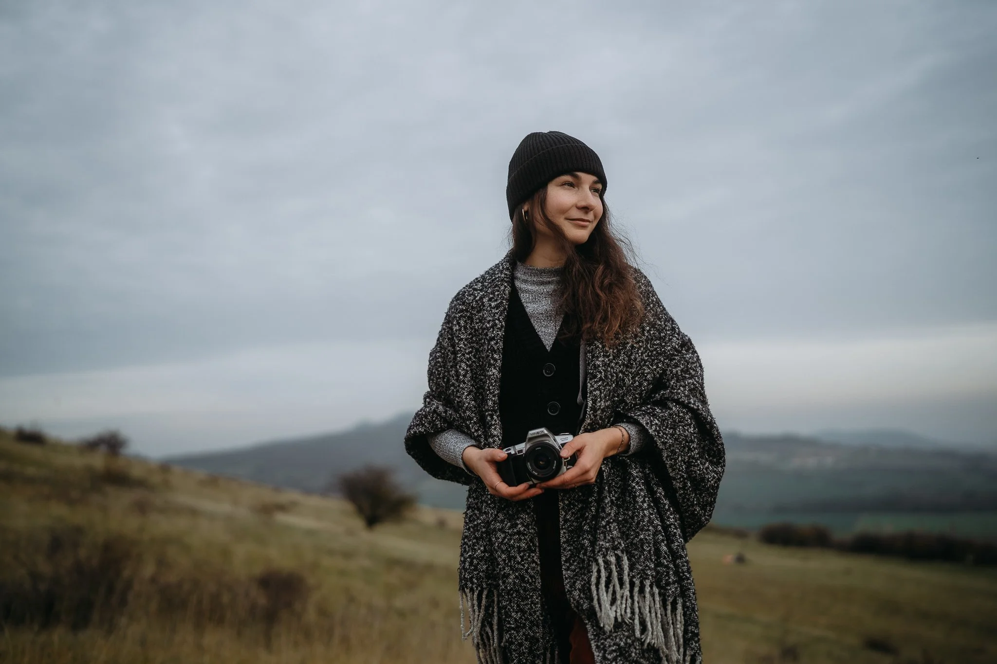 Portrét fotografky na Rané v Českém Středohoří, která se prochází přírodou. Obloha je zatažená a podzimní krajina dodává trochu moody atmosféry.