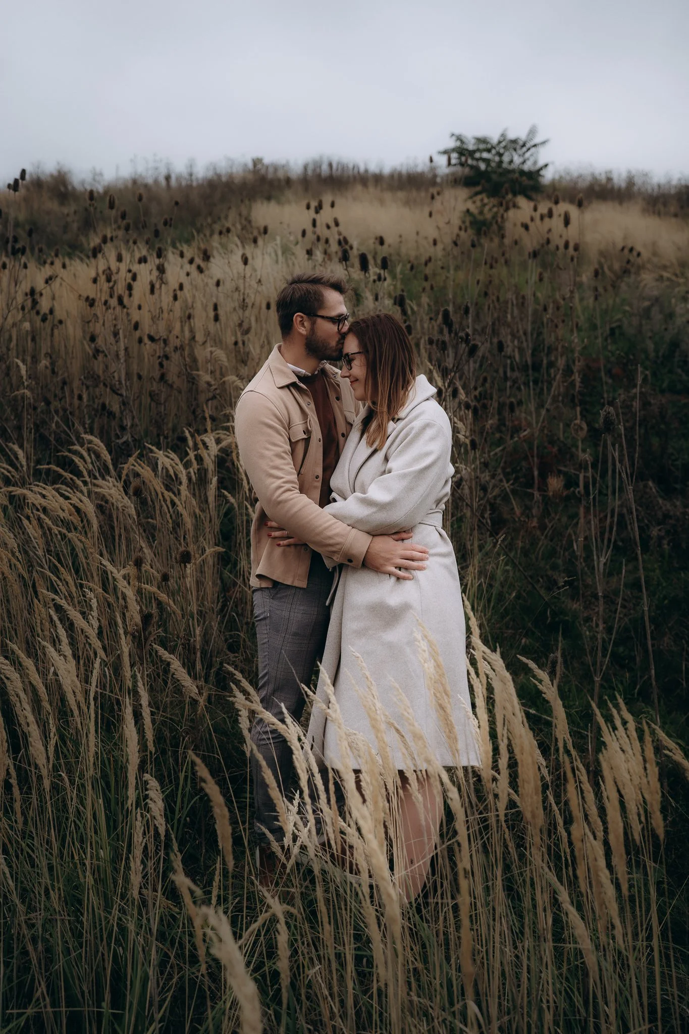 Párové focení v přírodě u Prahy – pár se objímá v podzimní trávě při zamračeném počasí. Lifestyle focení od fotografky Moniky Křenové.