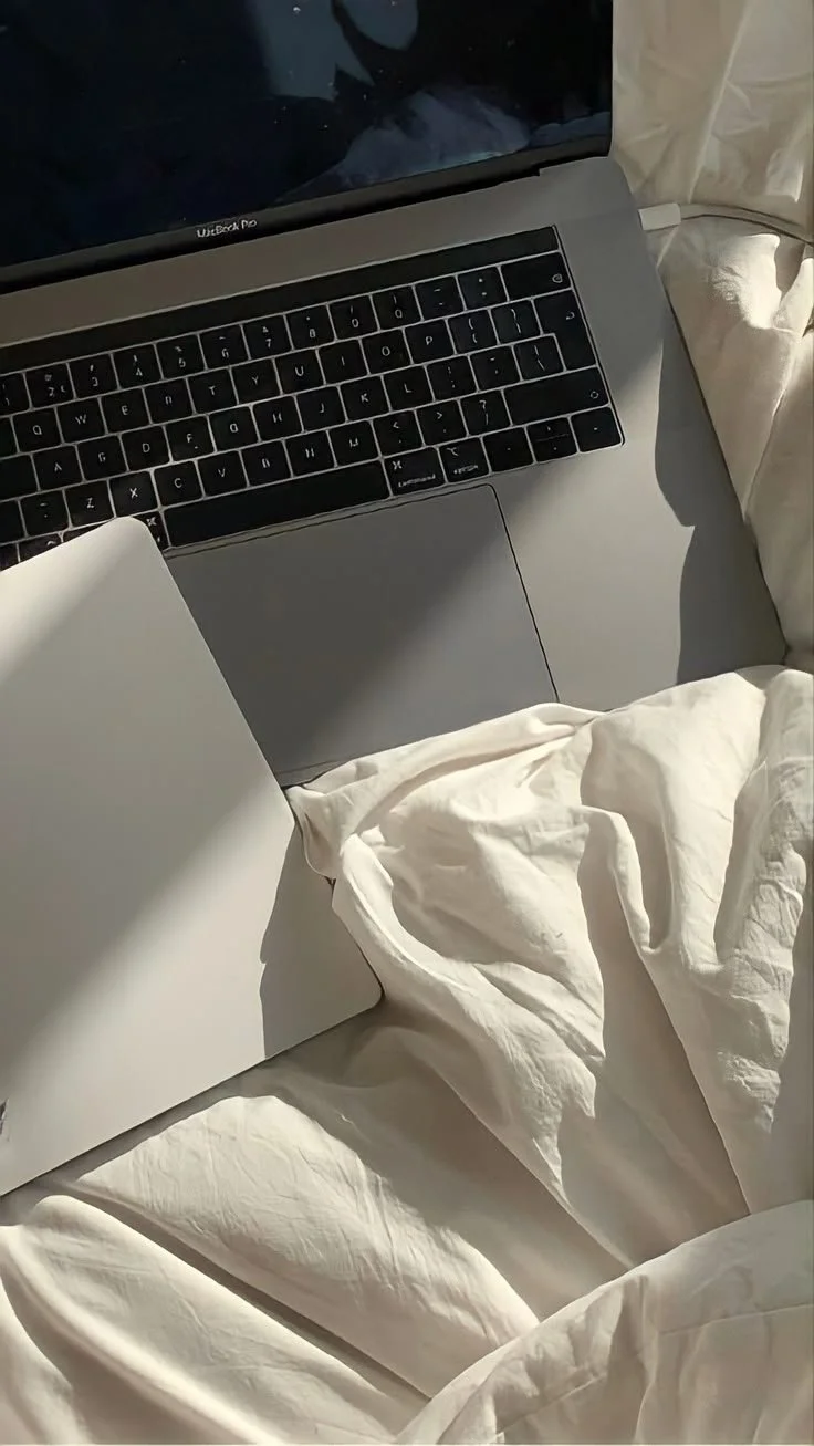 A laptop laying in white bed sheets.