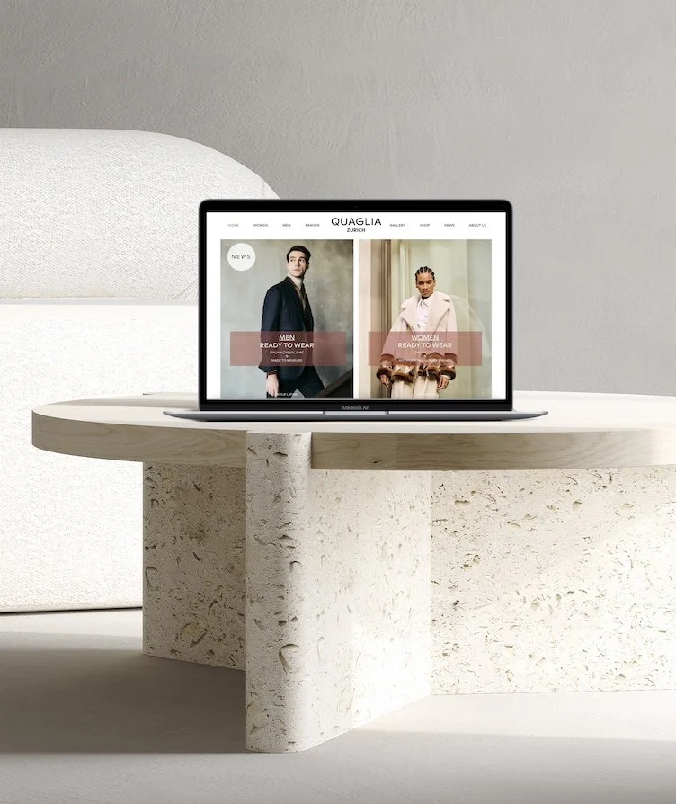 Laptop displaying a fashion website with men's and women's ready-to-wear sections, placed on a beige textured round table.