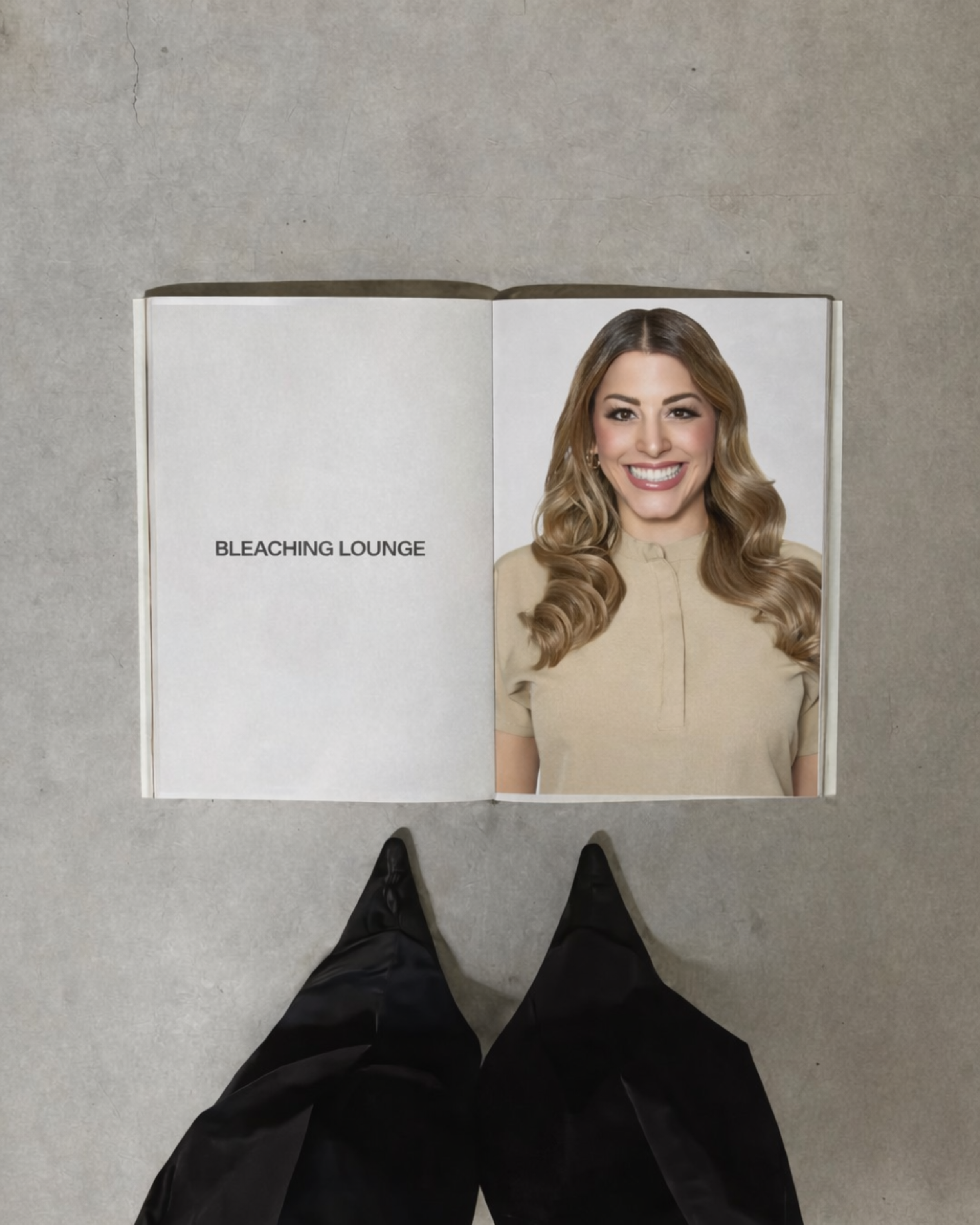 Open magazine showing a smiling woman with long wavy hair and a beige top, on a gray surface, with black shoes and pants visible at the bottom of the image.