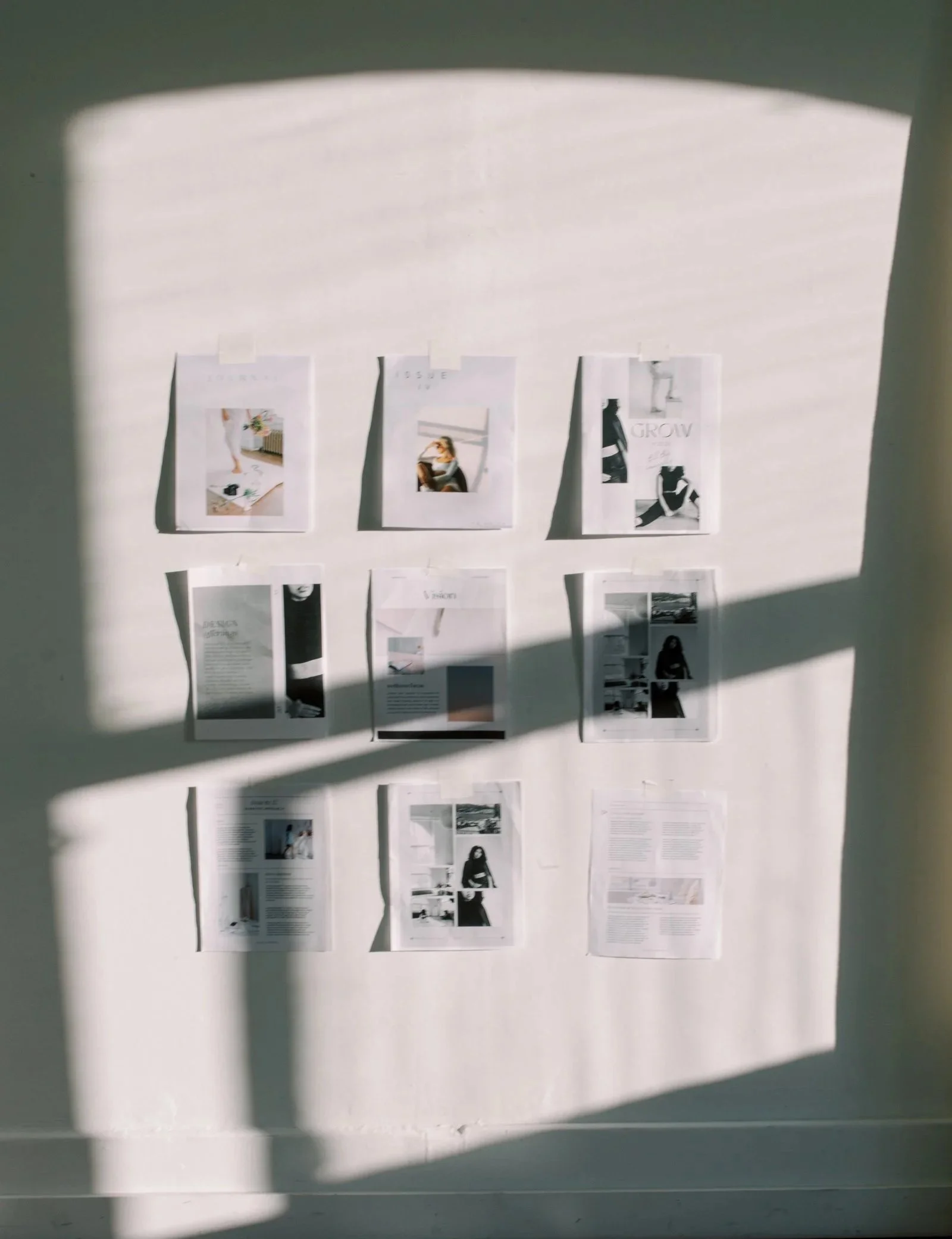 A wall displaying various printed pages with images and text, shadowed by window blinds.